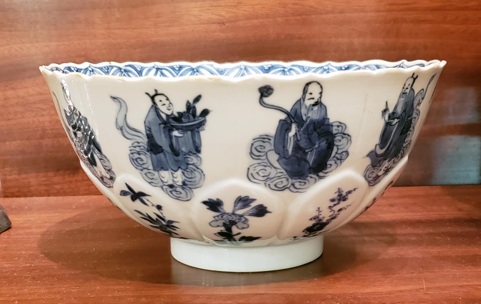 Kangxi period Chinese blue and white bowl,
The Eight Immortals, the Three Star Gods and the goddess Xiwangmu,
circa 1700.

The circular bowl with a petal-shaped moulded lower section, each petal with a painted plant. The upper section with a