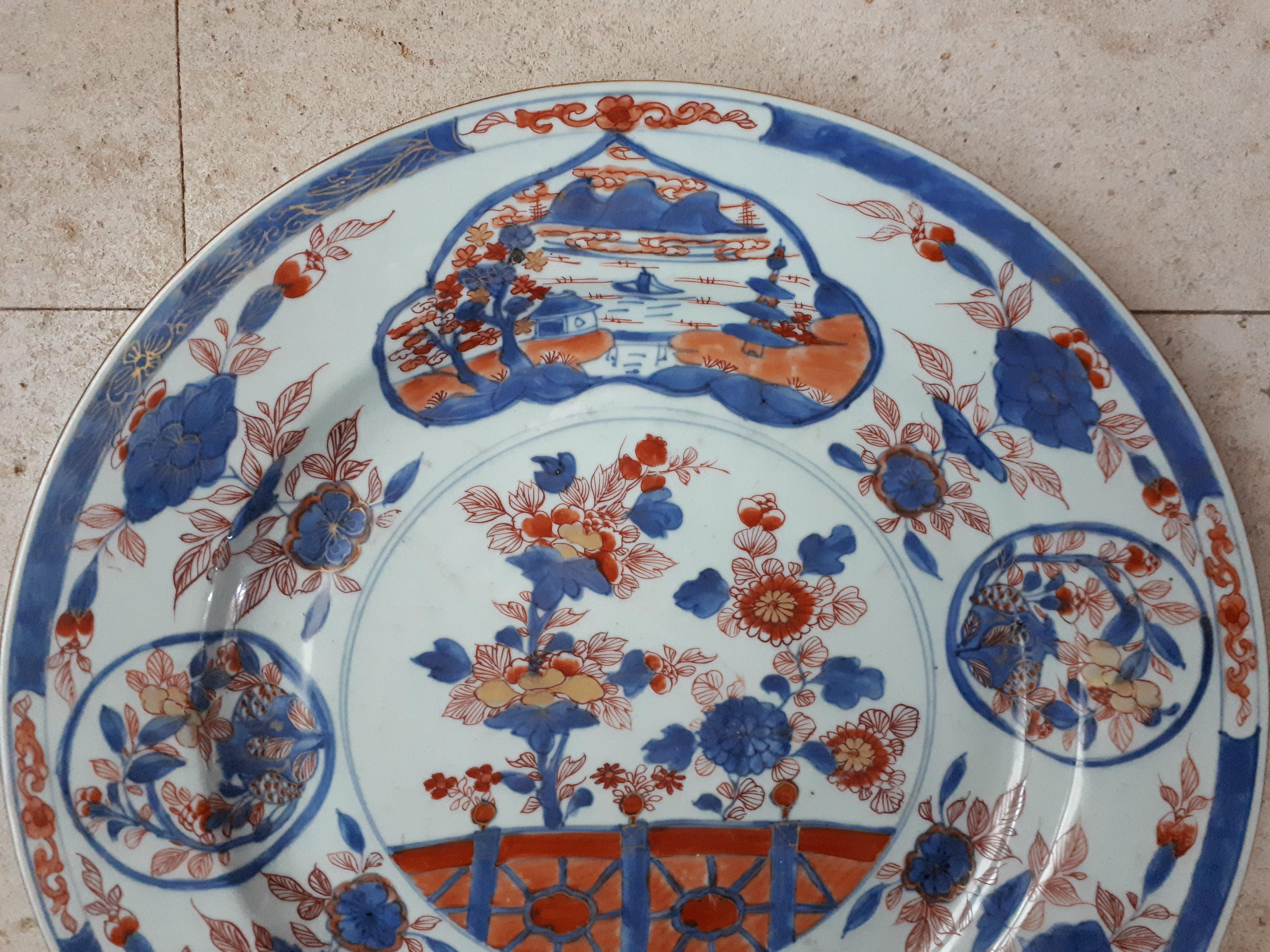 Plat en porcelaine décoré en bleu et rouge de fer avec des rehauts dorés de fleurs et de paysages. Un éclat à peine visible sinon superbe état de conservation. Diamètre : 39 cm. Marqué d'un lingzhi dans un double cercle, période Kangxi.