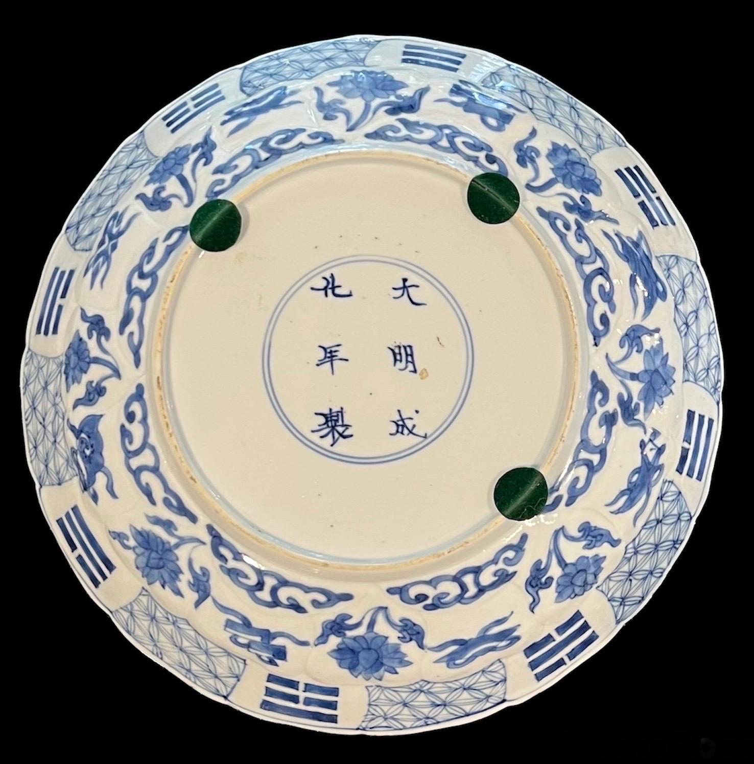 Kangxi period molded blue & white dish
The center painted with 2 figures in an 
Interior with molded foliage medallion surrounded by 
Flower sprigs alternating with the ba jixiang in molded 
Petal reserves in the well, base with six character