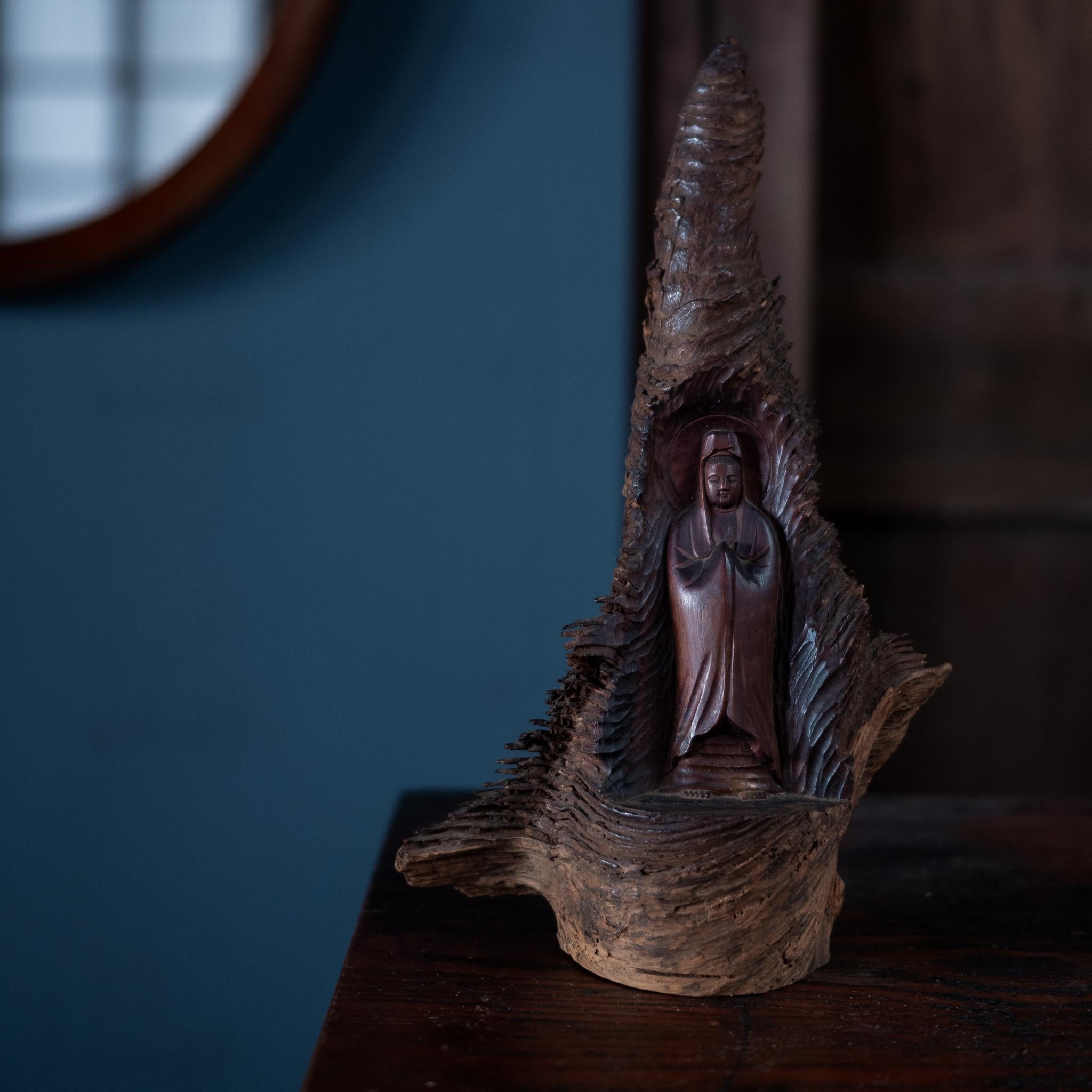 An evocative and beautifully hand-carved wooden sculpture of Kannon, delicately enshrined within a natural bark-like form. This piece blends devotional reverence with organic artistry.

The gentle figure of Kannon stands in a quiet pose, symbolizing