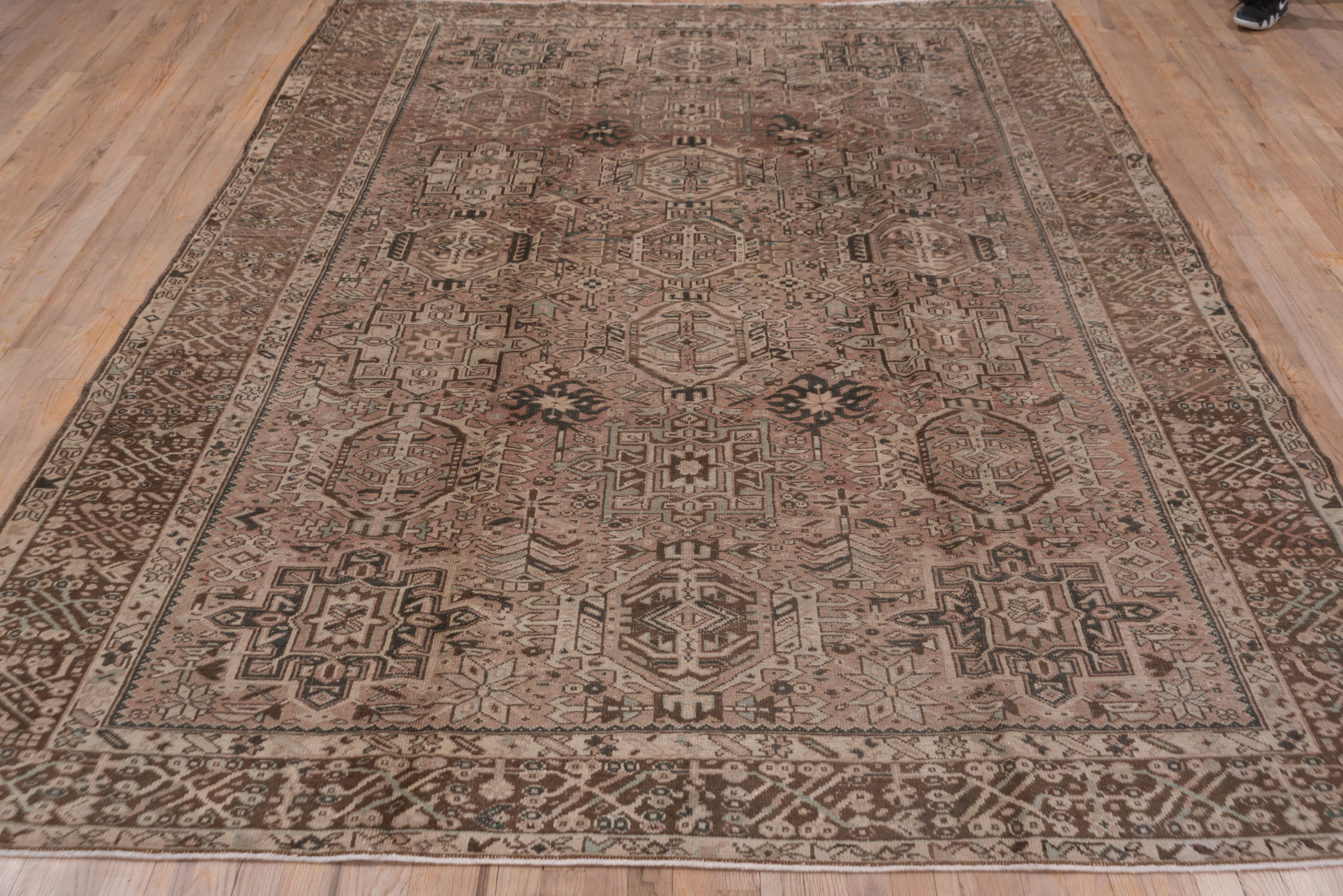 The buff field of this NW Persian village carpet displays three columns of characteristic Karaja octogramme and hooked hexagon medallions, all within a square bud-spray module repeat on the sienna brown border.