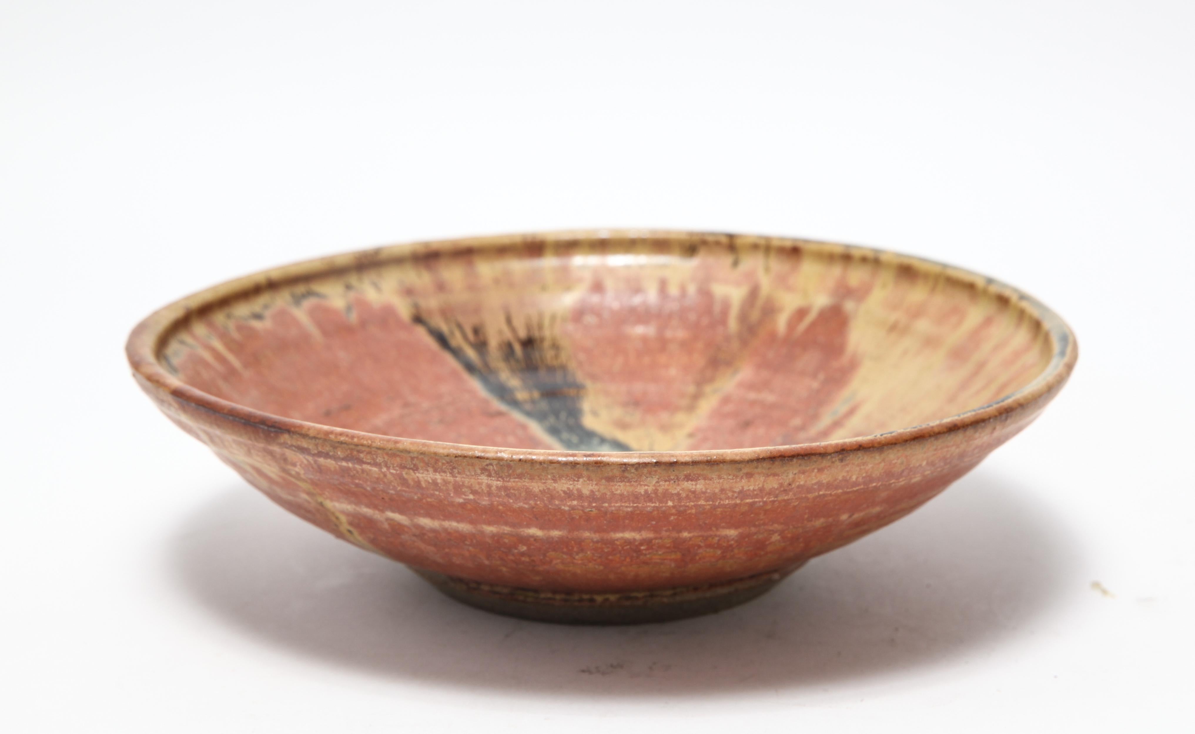 American Mid-Century Modern stoneware art pottery footed bowl designed by Karen Karnes (American, 1925-2016) with burnt orange, ochre, and brown glazes. The piece is signed with an impressed artist's monogram 