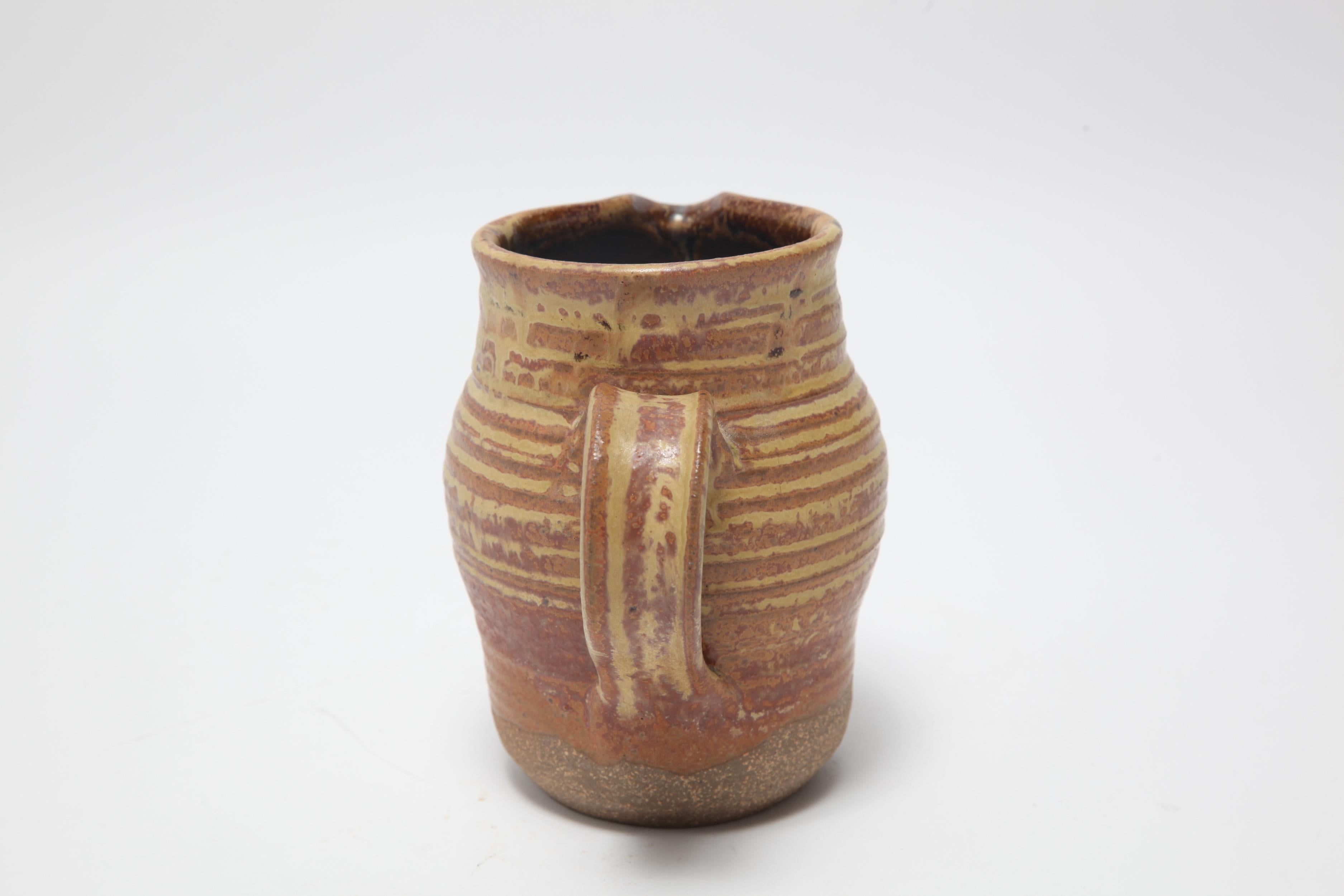 American Mid-Century Modern stoneware art pottery pitcher designed by Karen Karnes (American, 1925-2016), with an orange and ochre glaze. The piece is signed with an impressed artist's monogram 