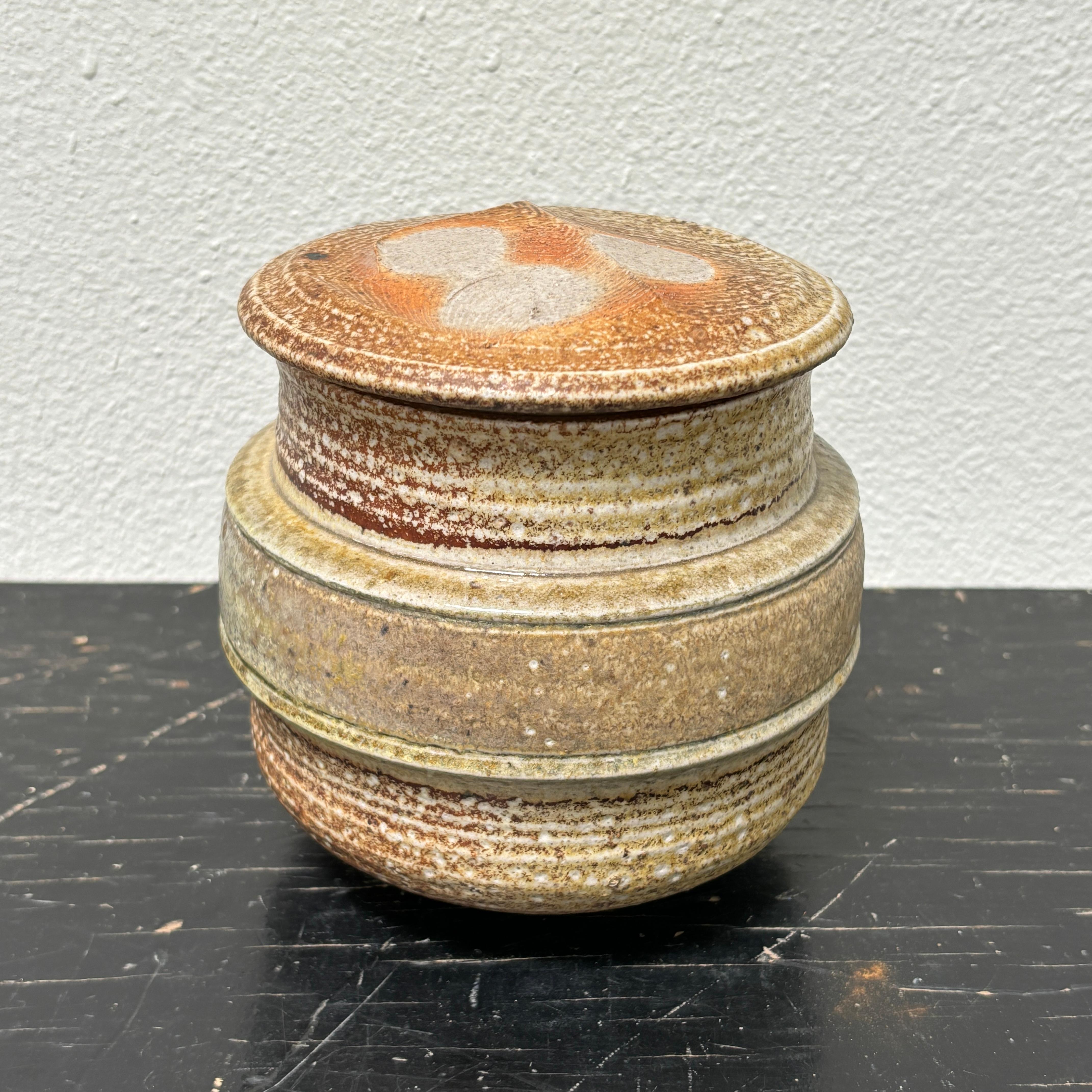 Karen Karnes salt glazed jar w/ lid.

A standard format for the artist, this particular piece is a great example, solid and well executed some great details in the glazing, fading and a variance of oranges, browns and beige tones.
The form has