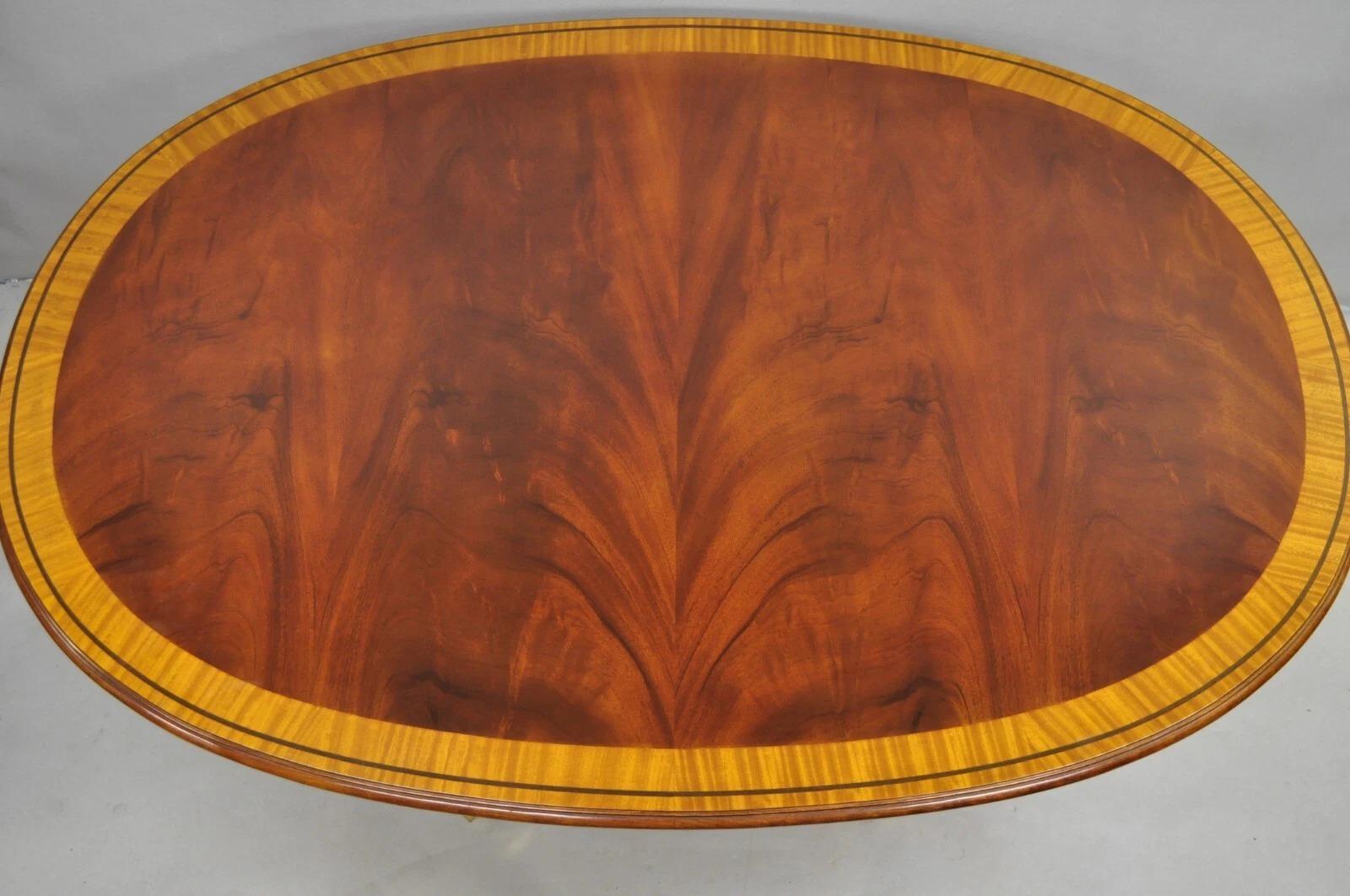 Karges English Duncan Phyfe Style Satinwood Banded Inlay Crotch Mahogany Oval Dining Table with Brass Capped Rolling Casters. Top is solid and does not extend. Circa Late 20th Century. Measurements: 28.25