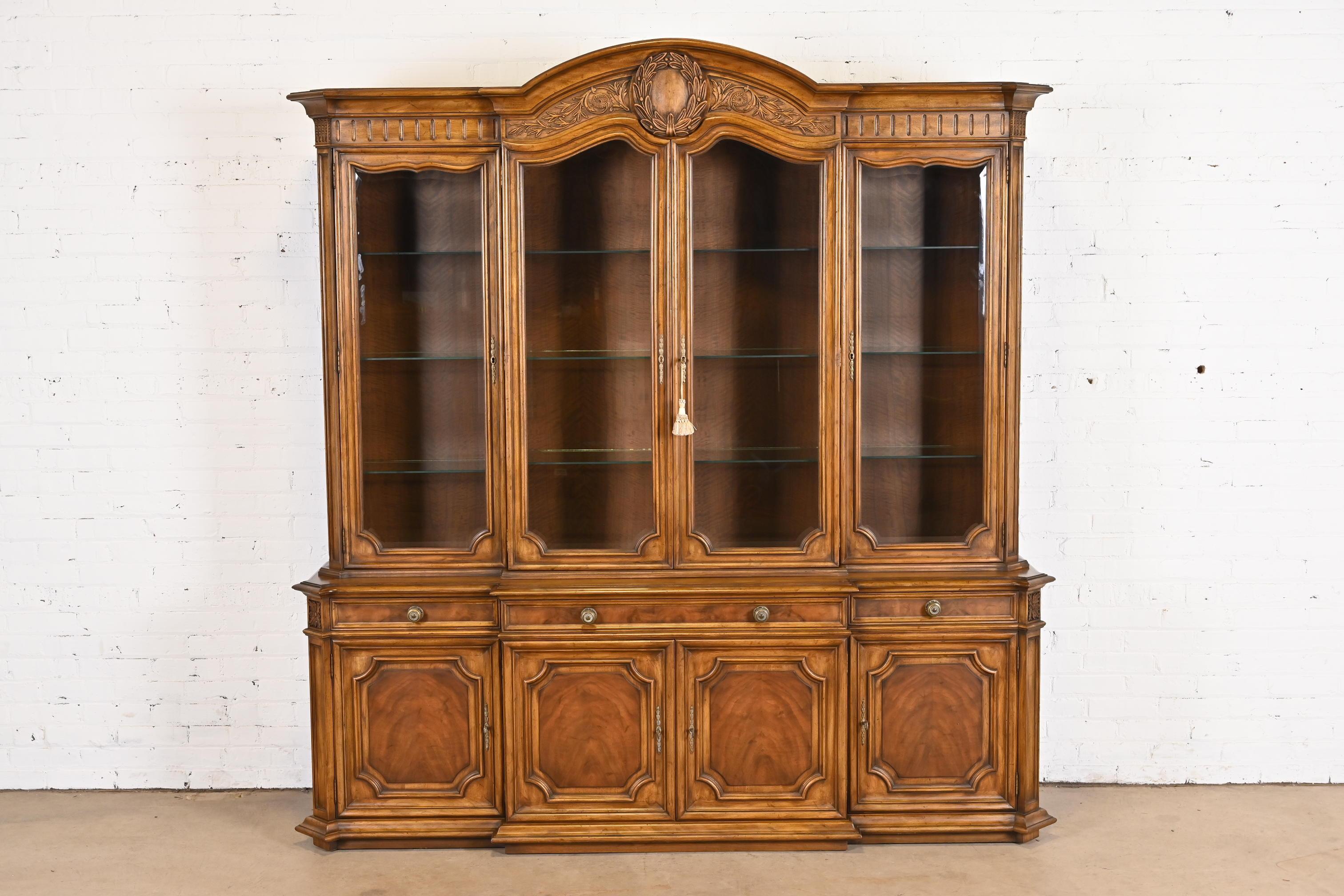 A gorgeous French Regency Louis XVI style lighted breakfront bookcase or dining cabinet

By Karges

USA, Circa 1960s

Carved burled walnut, with glass front doors and original brass hardware.

Measures: 80.5