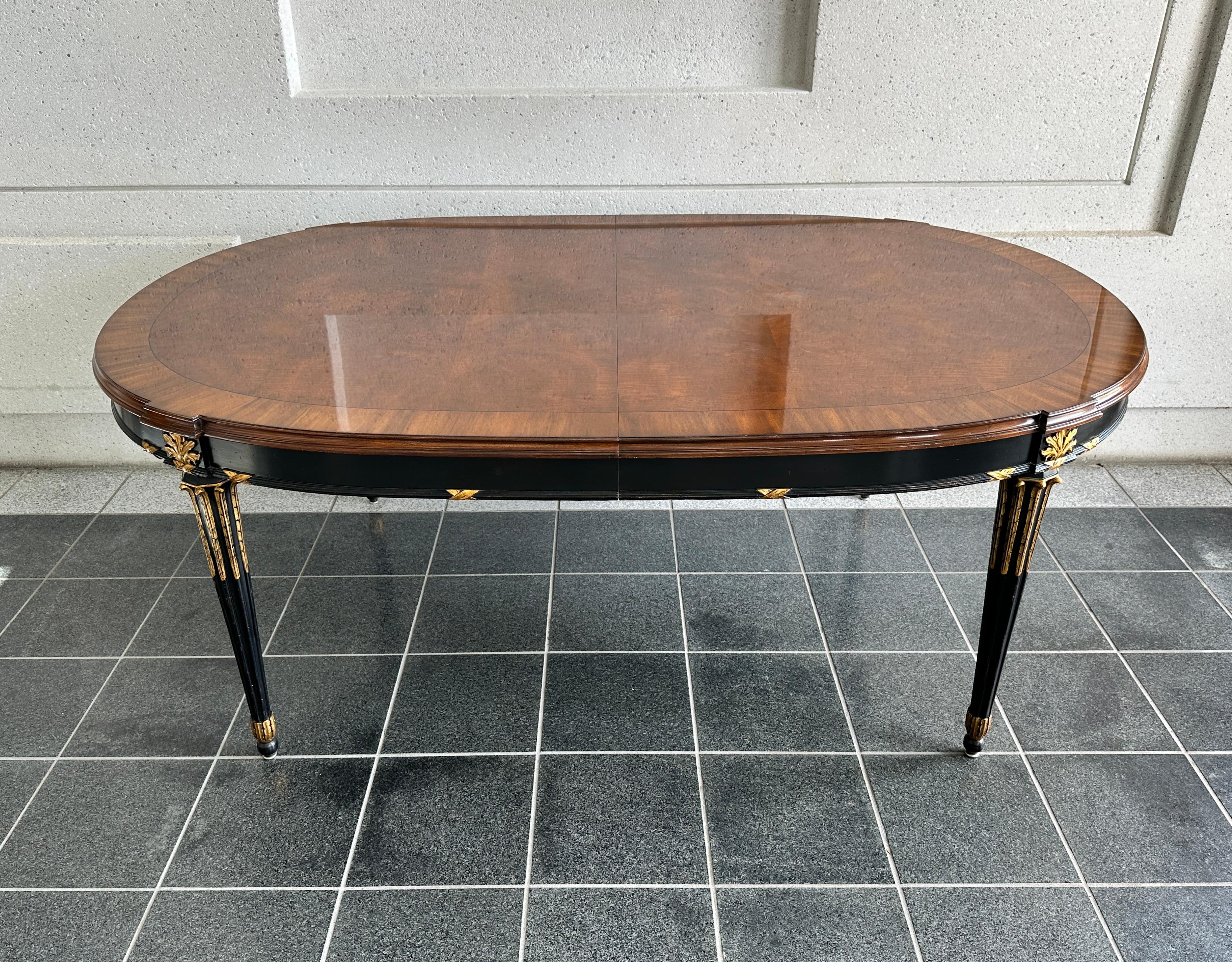 An exceptional French Regency Louis XVI style ebonized and gilt extension dining table by Karges Furniture USA, Circa 1990s. Gorgeous book-matched burled walnut top, with carved and tapered legs, and gold gilt wood details.  
This American Classical