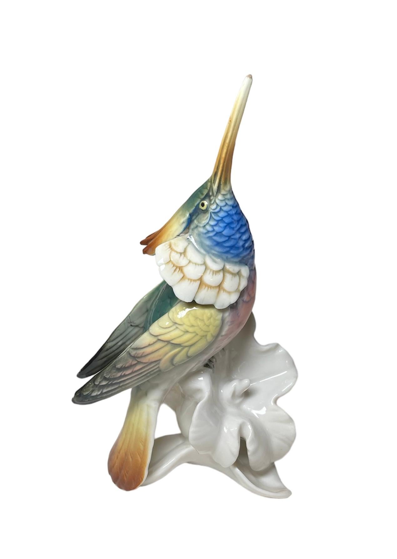 This is a Karl Ens Porcelain Factory bird figurine. It depicts a colorful hummingbird standing over an Hibiscus flower like and looking up to the sky. He is very proud to show his long beak. Below the base, it is the Karl Ens Porcelain Factory