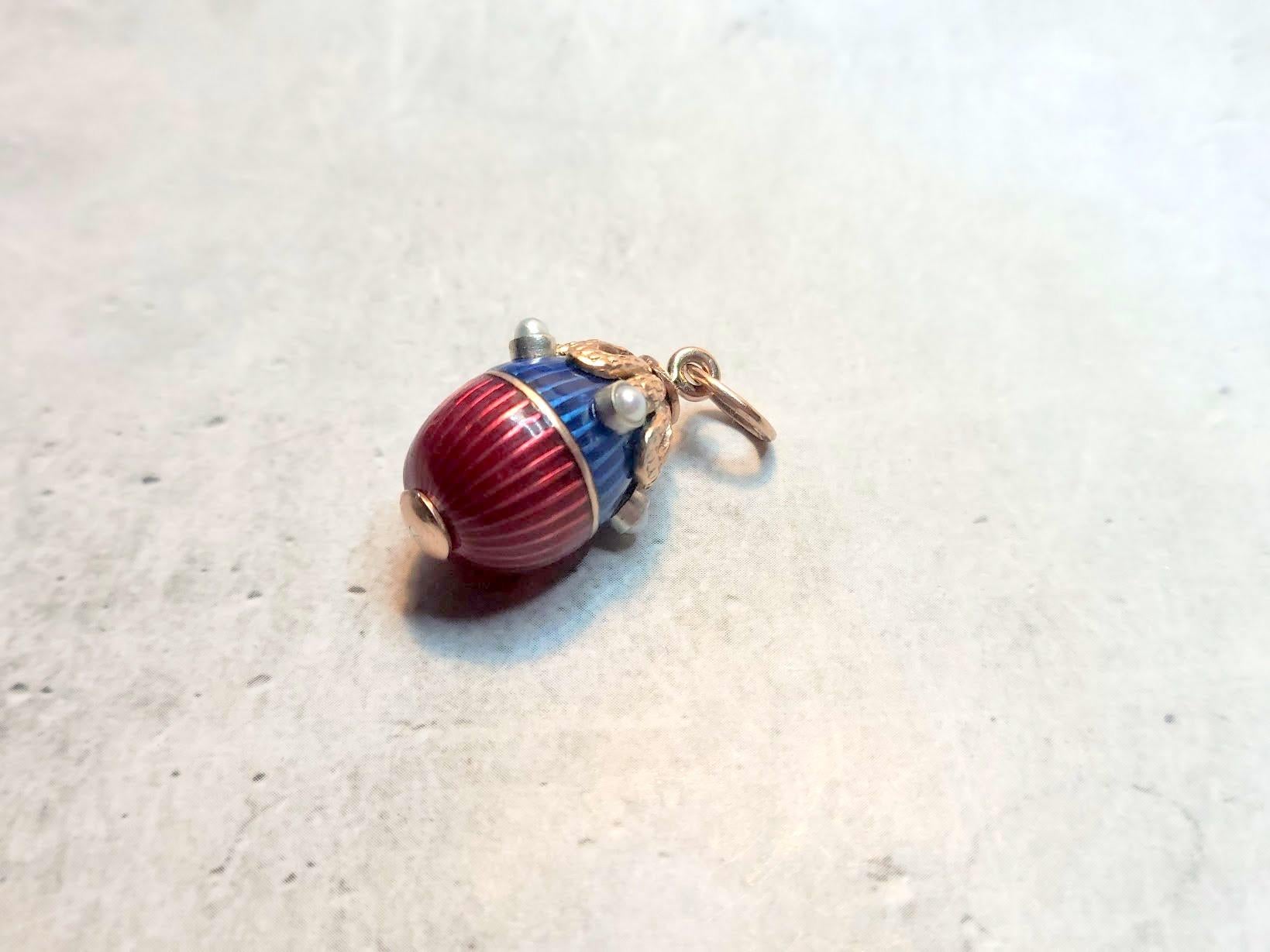We are delighted to present to you a rare and enchanting treasure from our collection — a miniature gold egg pendant by the legendary Karl Fabergé. This exquisite piece is adorned with deep blue and rich red enamel, delicately framed with rose gold,