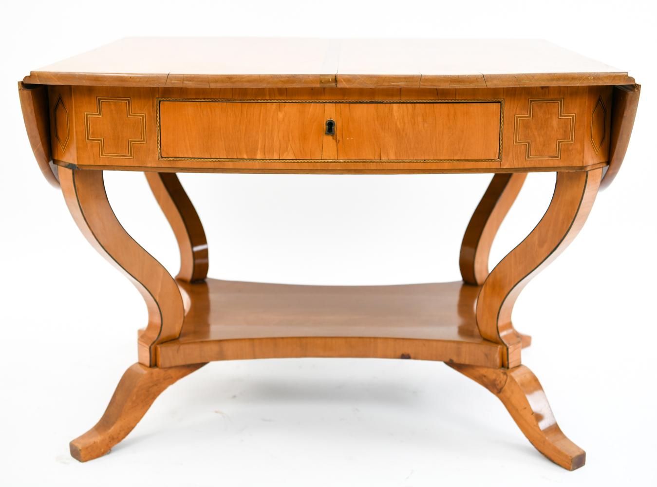 This is a handsome antique Danish Biedermeier birch desk with drop leaves. This desk features a cross motif on either side of the drawer and sits upon gracefully curved legs. This piece is in the style of Karl Johan.