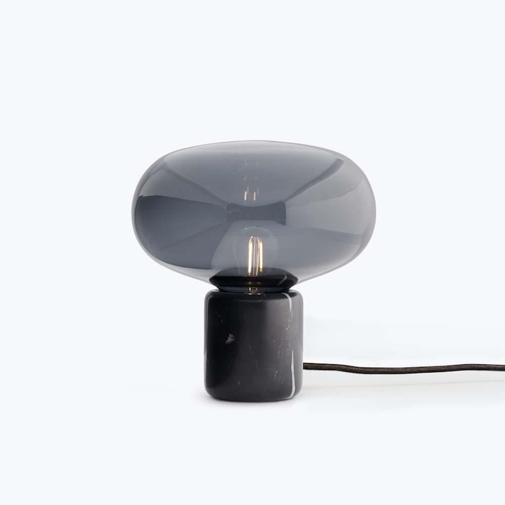 The Karl-Johan table lamp is inspired by excursions into nature. A search for wild mushrooms. The tones of an autumn forest. This soothing lamp combines the soft curves of glass with the stability of black marquina or smoked oak. The result is a