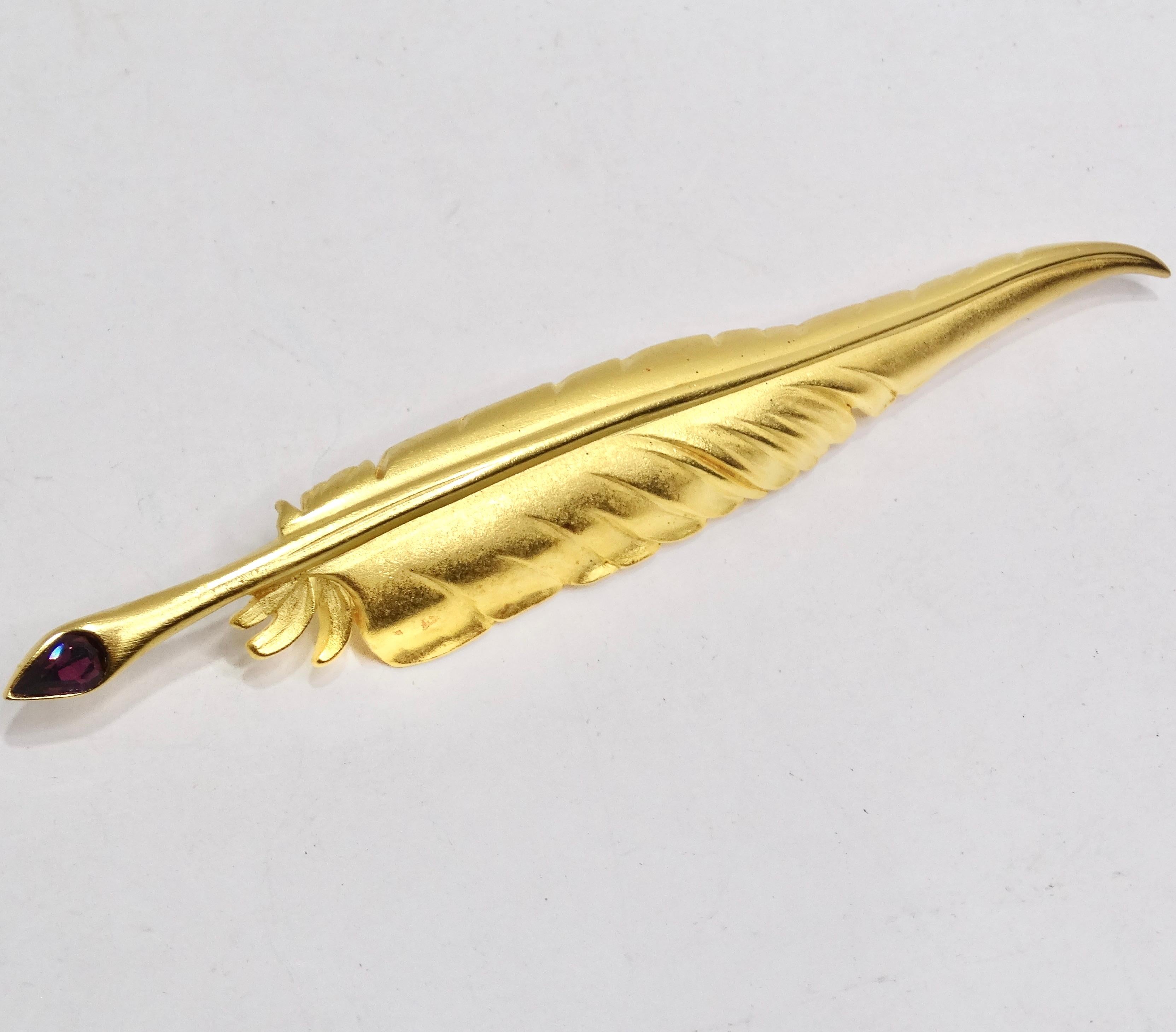 Introducing the Karl Lagerfeld 1980s Gold Plated Purple Gem Feather Brooch – a stunning statement piece that embodies chic elegance. This shiny yellow gold plated brooch is crafted in a sleek feather shape, featuring a captivating purple gem at the