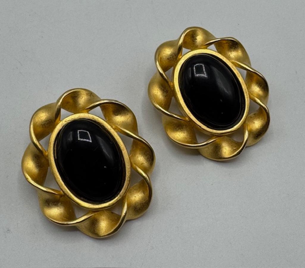 Un paio di orecchini a bottone a clip vintage anni '80 di Karl Lagerfeld, con audaci centri ovali di cabochon neri incorniciati da uno scultoreo bordo a nastro ritorto color oro. 
Ogni orecchino con chiusura a clip misura 1,5