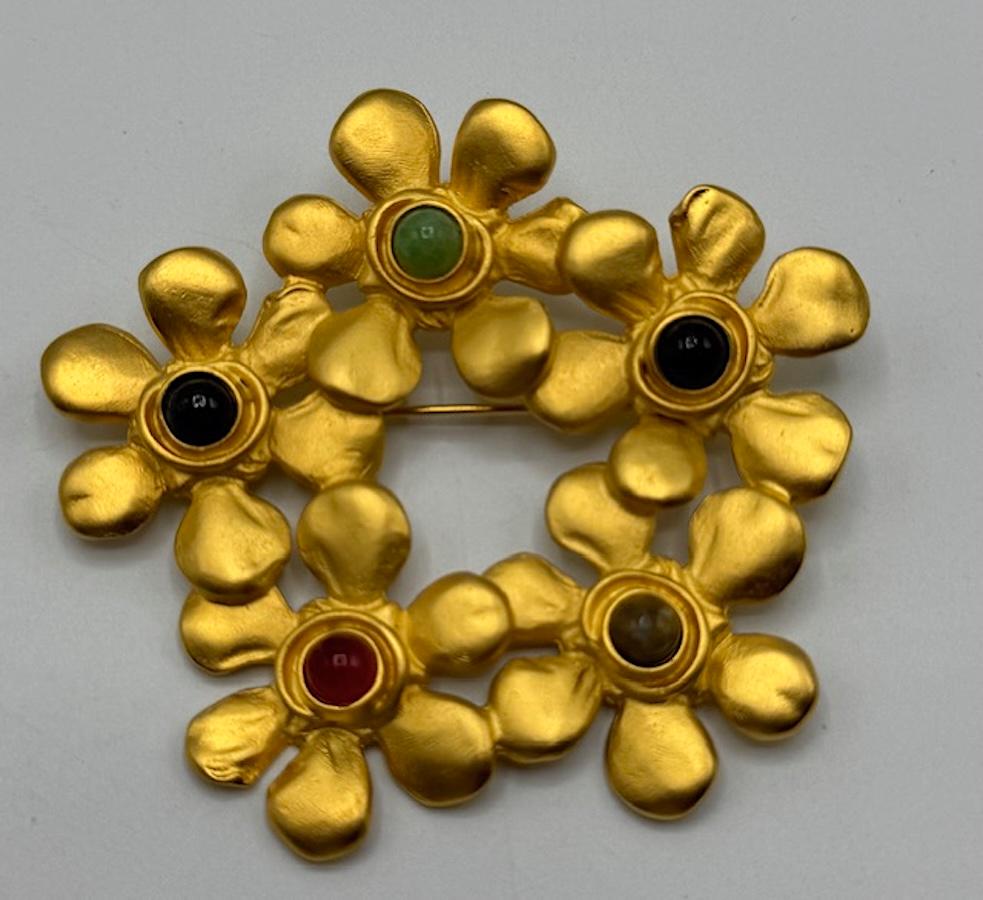 Questa straordinaria spilla vintage di Karl Lagerfeld, risalente agli anni '80, presenta un audace motivo floreale realizzato in metallo dorato. Ogni fiore è centrato da un cabochon rotondo in vibranti tonalità Jewell di verde, rosso e nero, che