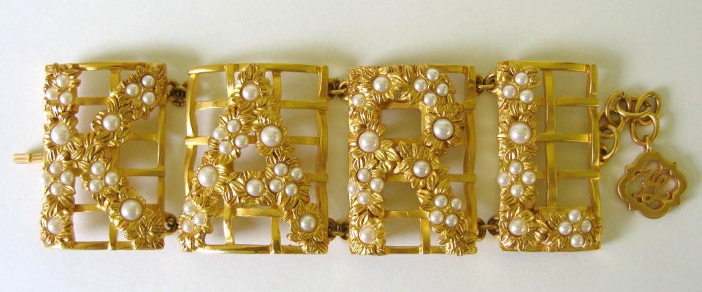 This fabulous link bracelet is designed in 4 panels that spell out KARL. A trellis is formed as a background for the flowering vines that grow. White glass pearls form the center of flowers. The base metal is plated in 18K gold. Nothing but the