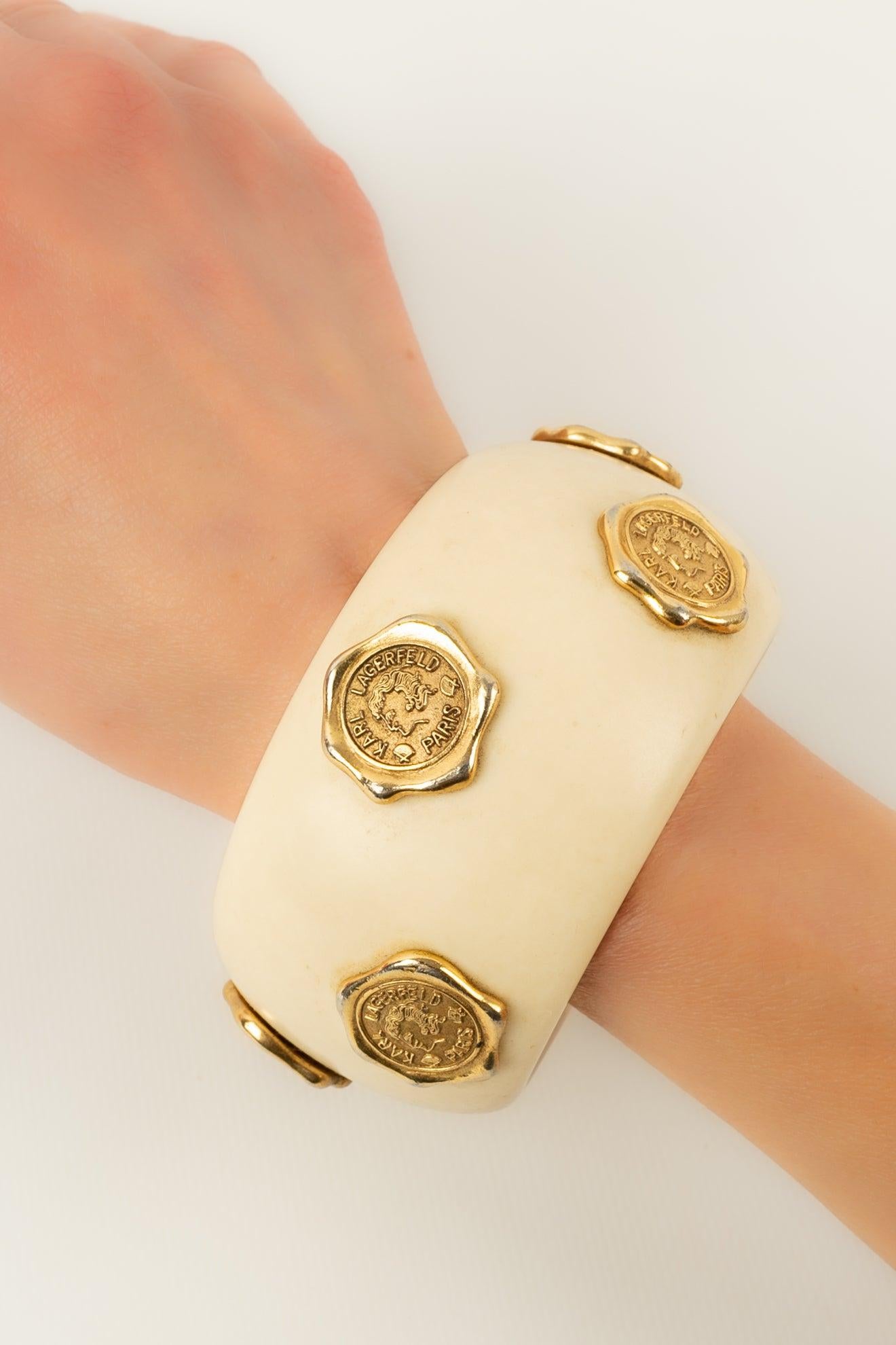 Lagerfeld - Cuff bracelet in beige bakelite ornamented with engraved pieces in gold-plated metal.

Additional information:
Condition: Good condition
Dimensions: Wrist circumference: 20 cm

Seller Reference: BRA176
