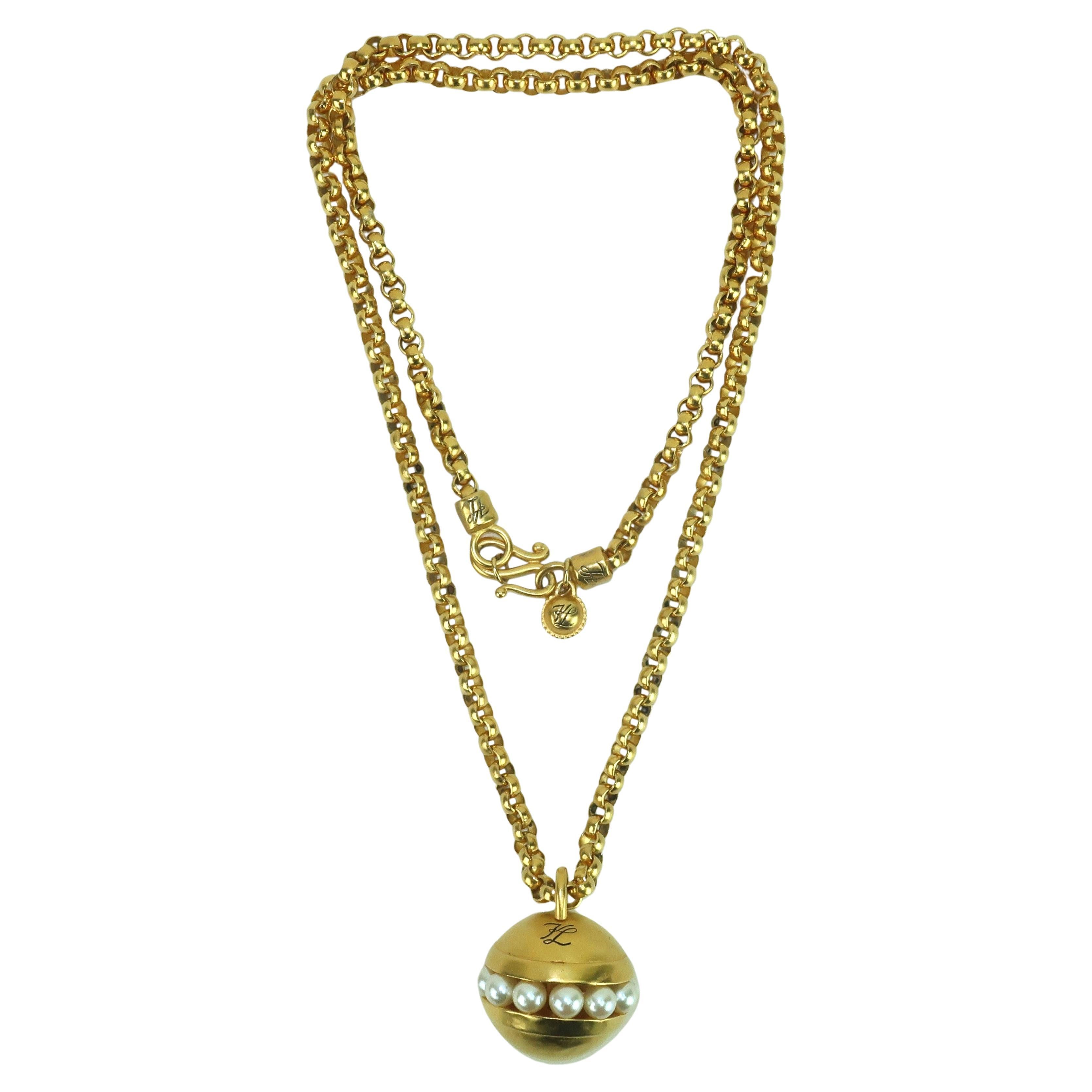 Una collana chic degli anni '80 di Karl Lagerfeld, composta da una catena dorata a lunghezza d'opera accompagnata da un ciondolo a forma di sfera impreziosito da perle finte.  Il logo 