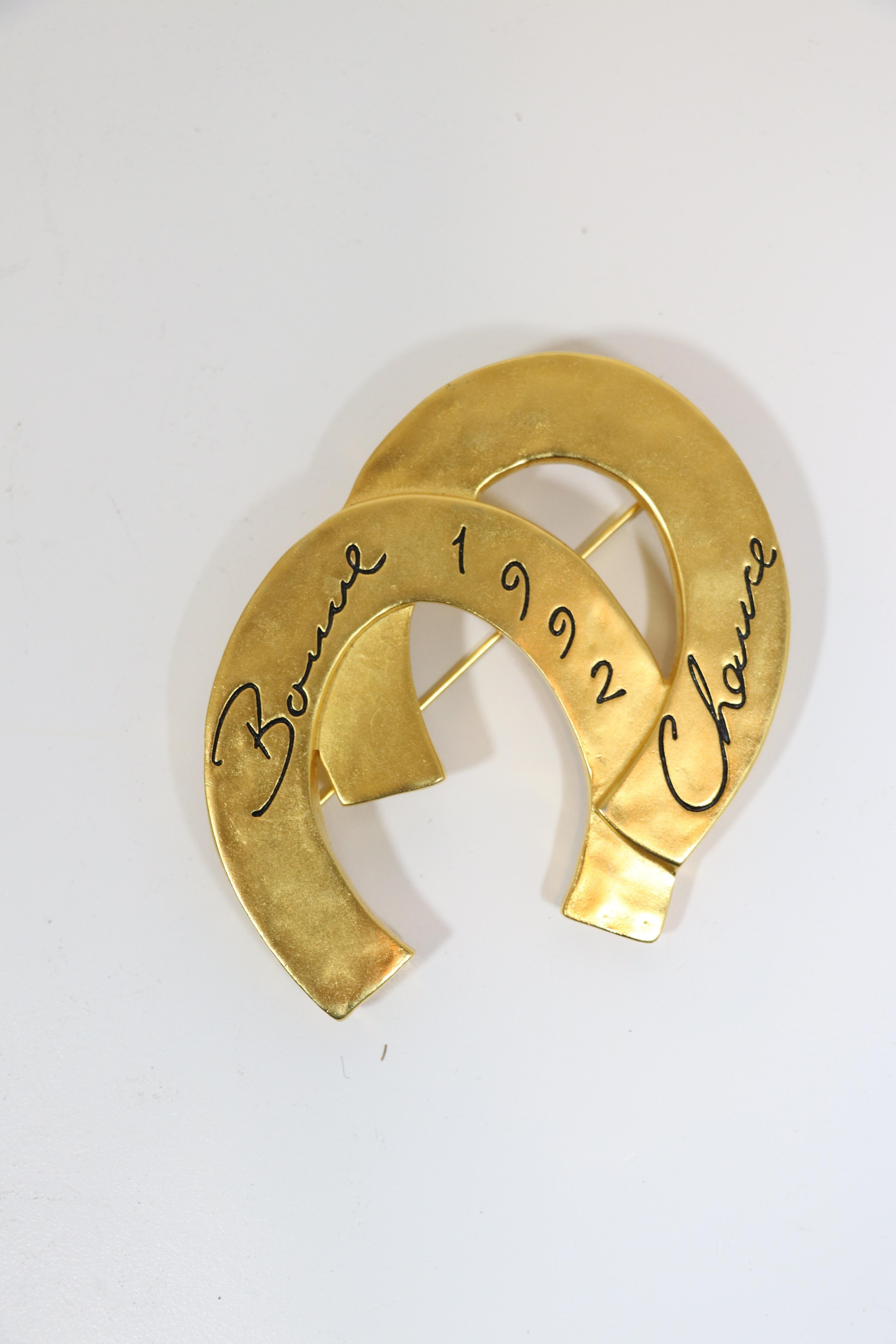 Massive brushed gold-tone vintage 1992 brooch by the late and iconic Karl Lagerfeld presents two massive horseshoes that say 