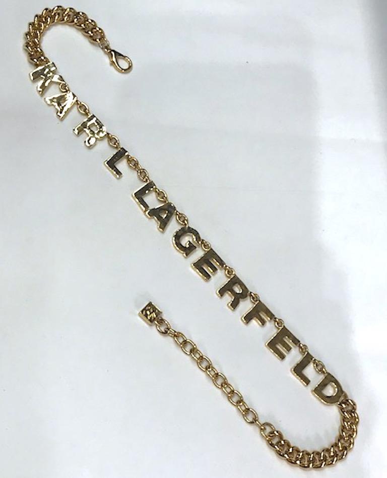 Karl Lagerfeld name necklace in bright gold. Each letter is .5 of an inch wide and .63 of an inch high with a light martele' texture. There are three inches of curb link chain on each end. There is a lobster claw clasp on one end and 2.75 inch
