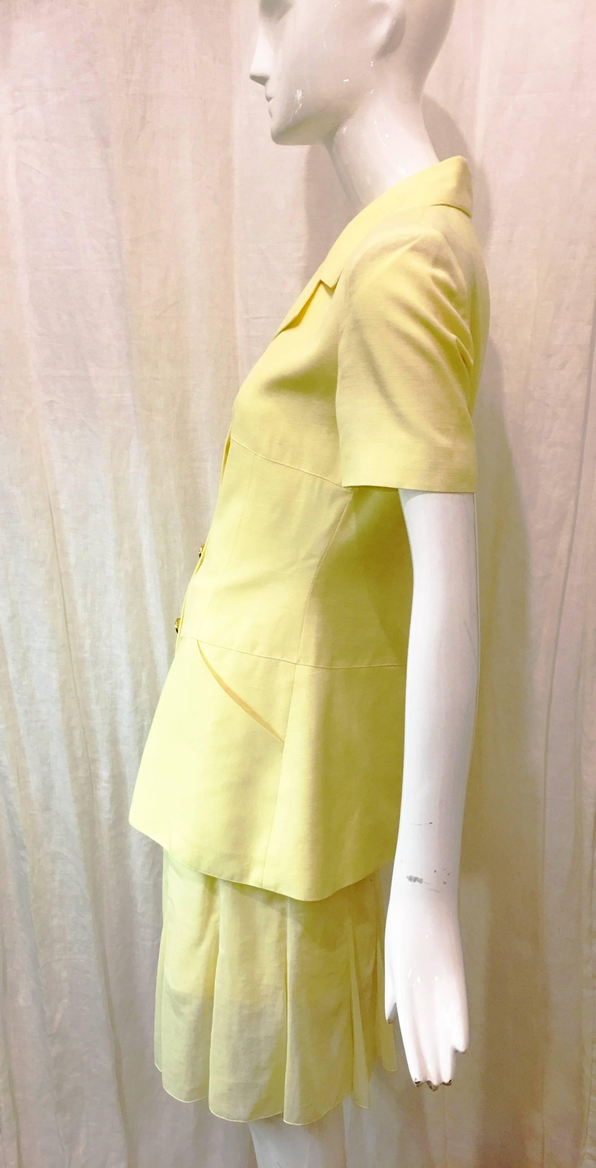 Pale yellow short sleeve suit jacket. Small shoulder pads add flattering silhouette (not overwhelming or bulky). Four gold tone star overlay buttons with yellow centers. Two angled pockets at front of garment. Stitching flatters the frame and adds a