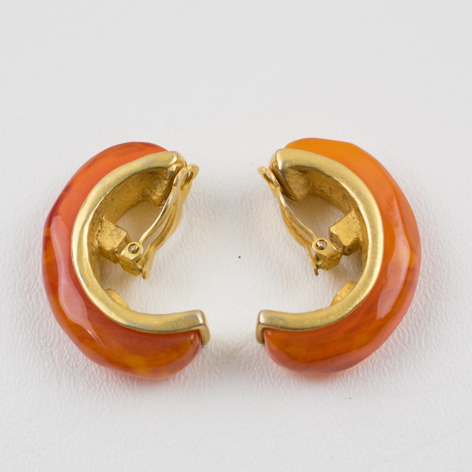 Exquisite Karl Lagerfeld Paris signed clip-on earrings. Large hoop shape with geometric design in brushed gilt metal, topped with carved, faceted orange marble resin ornament. Marked underside with the 
