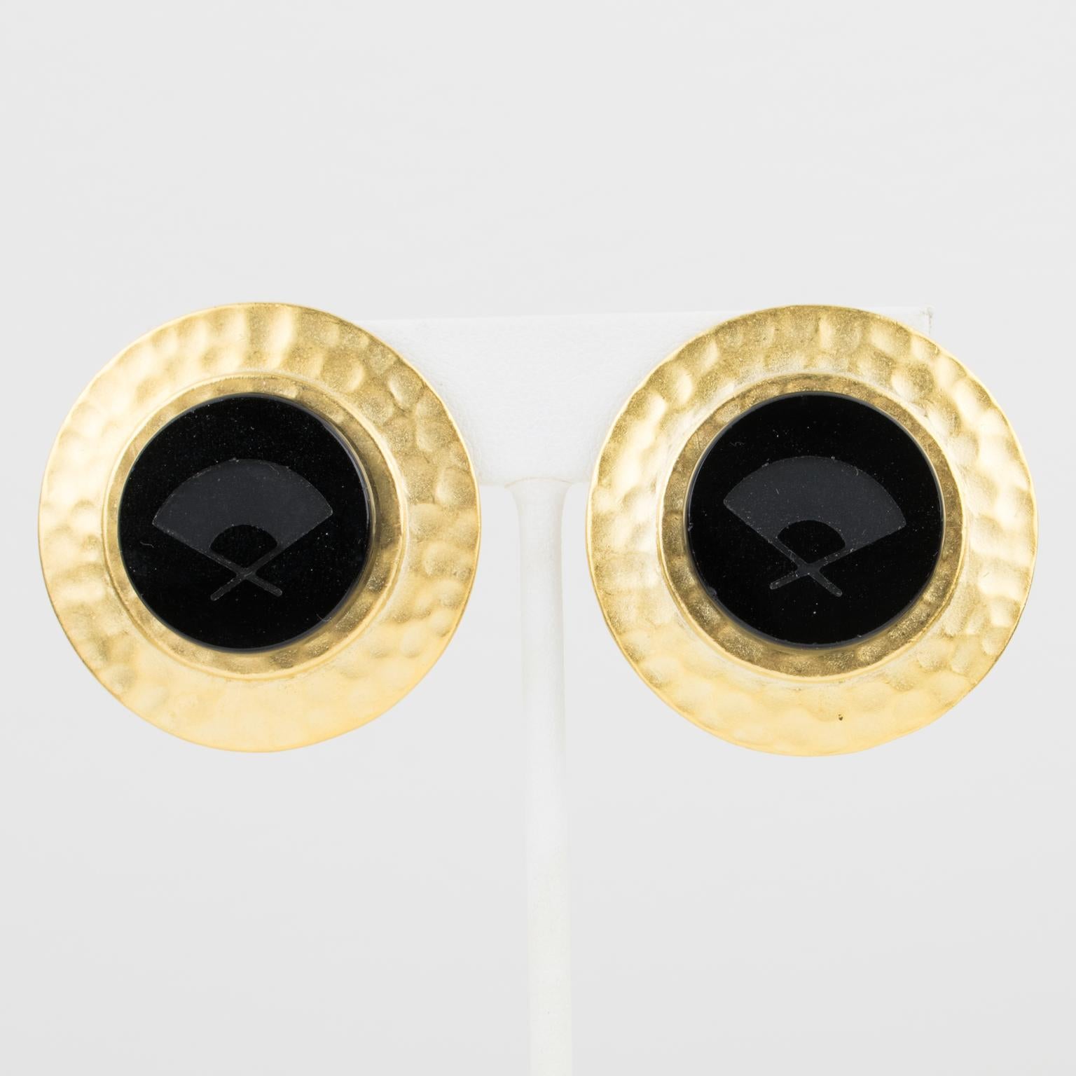 Karl Lagerfeld Paris ha disegnato questi deliziosi orecchini a clip. I pezzi sono caratterizzati da un'incorniciatura rotonda in metallo dorato con texture, sormontata da un'incisione in vetro nero ornata dal logo intagliato del ventaglio del