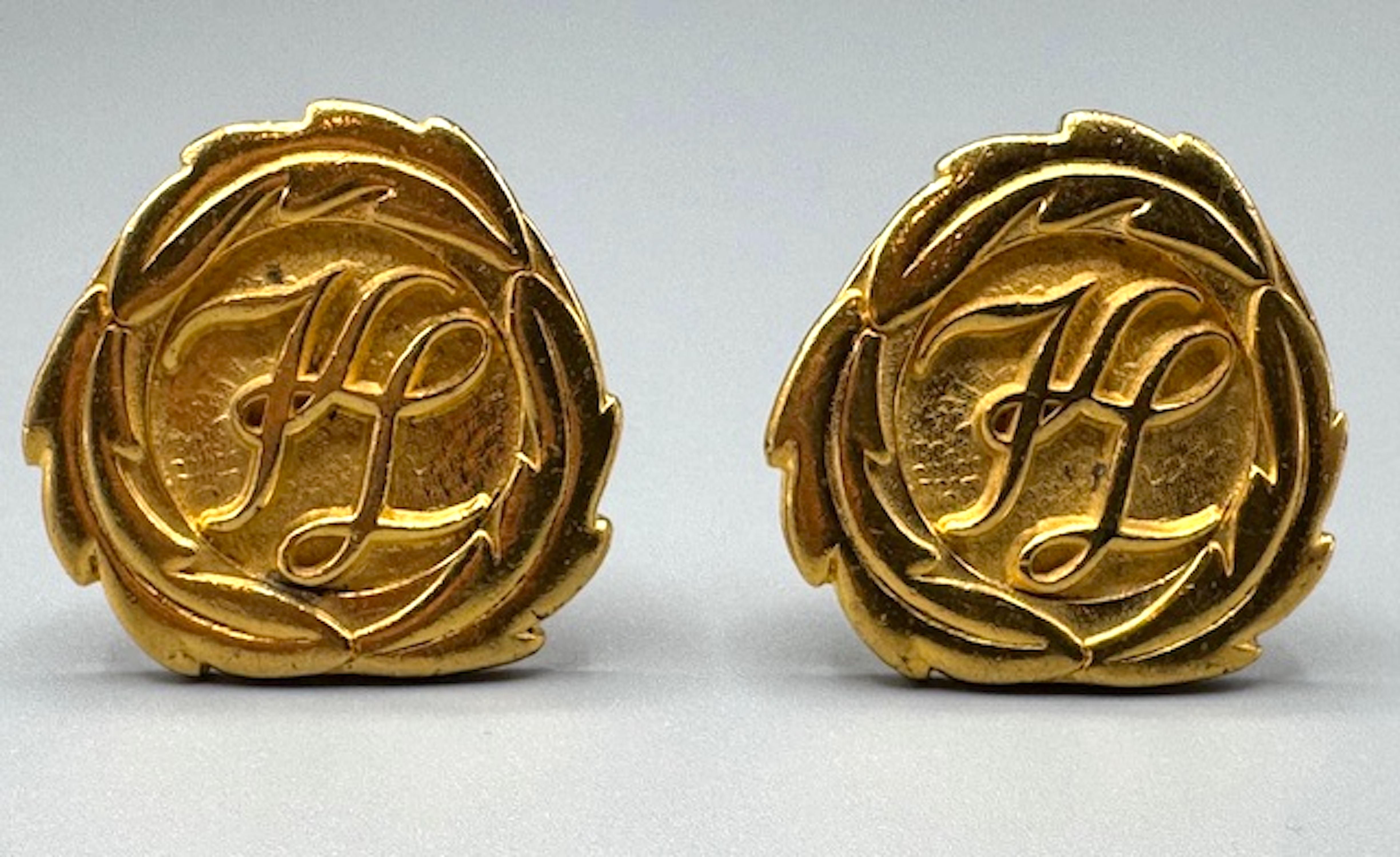 A wonderful pair of classical button earrings by Karl Lagerfeld from the 1980/90s. Each cast earring measures 1.38 inches in diameter, gold plated and features the famous KL interlocking script initial logo within a border of three long leaves. Clip