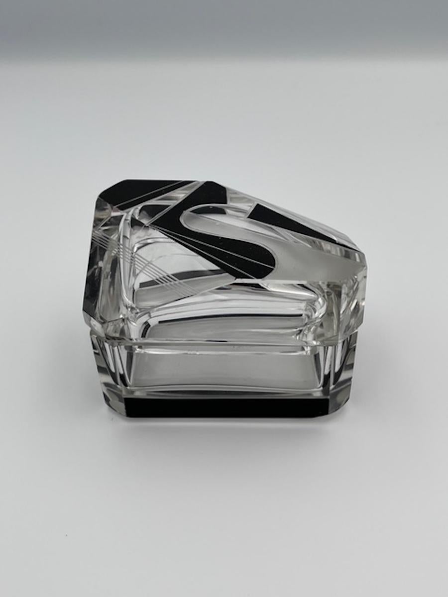 Esta impresionante pitillera Art Decó de Karl Palda es un excelente ejemplo del diseño checo en cristal de los años 30, con un elegante cuerpo rectangular y una tapa de cristal tallado abstraído. El motivo geométrico Art Déco se acentúa con grabados