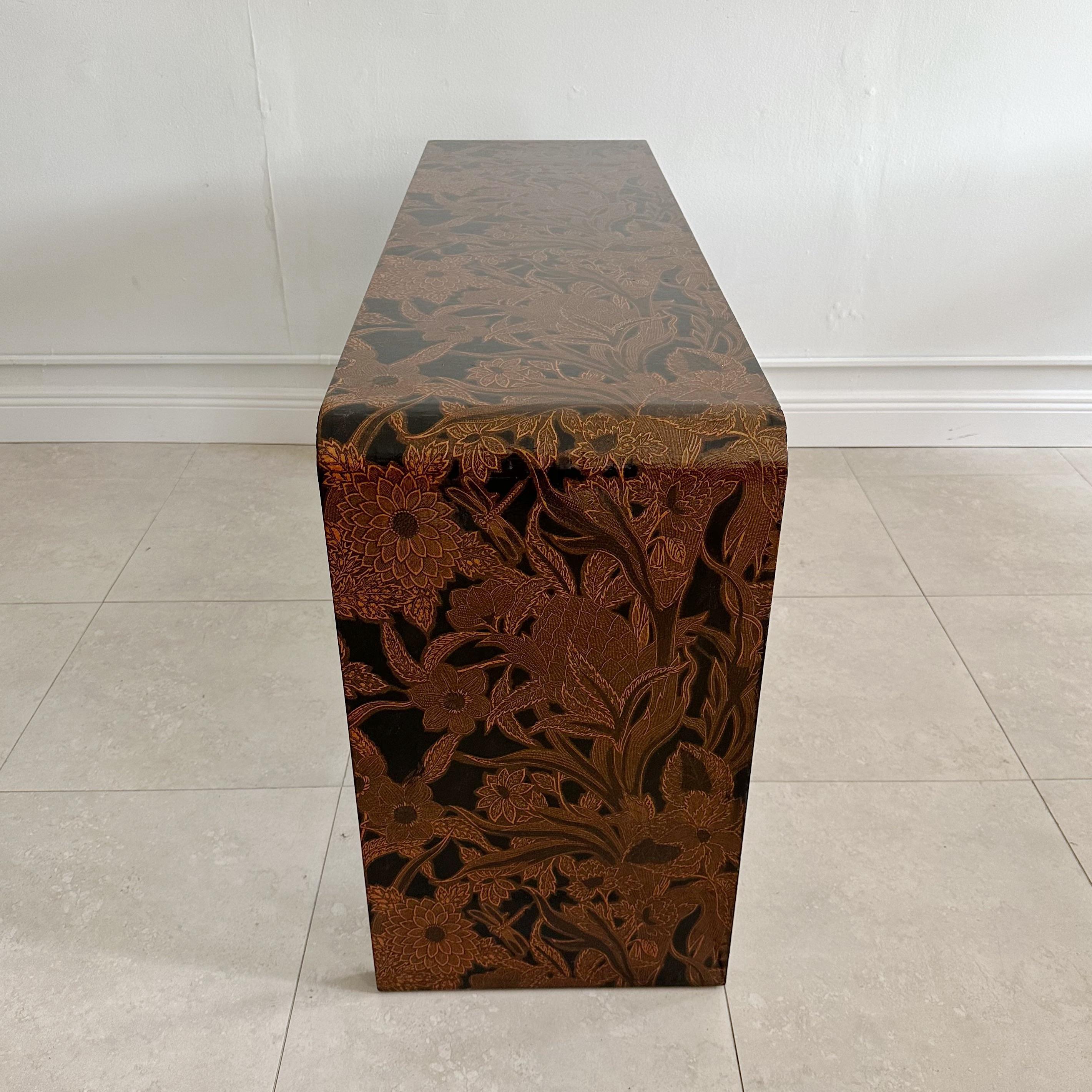 Karl Springer waterfall console table. Wrapped in a floral batik fabric and clear lacquered. American, 1970s. In excellent vintage condition with minor surface wear consistent with age and use. Knee hole measures 21.75