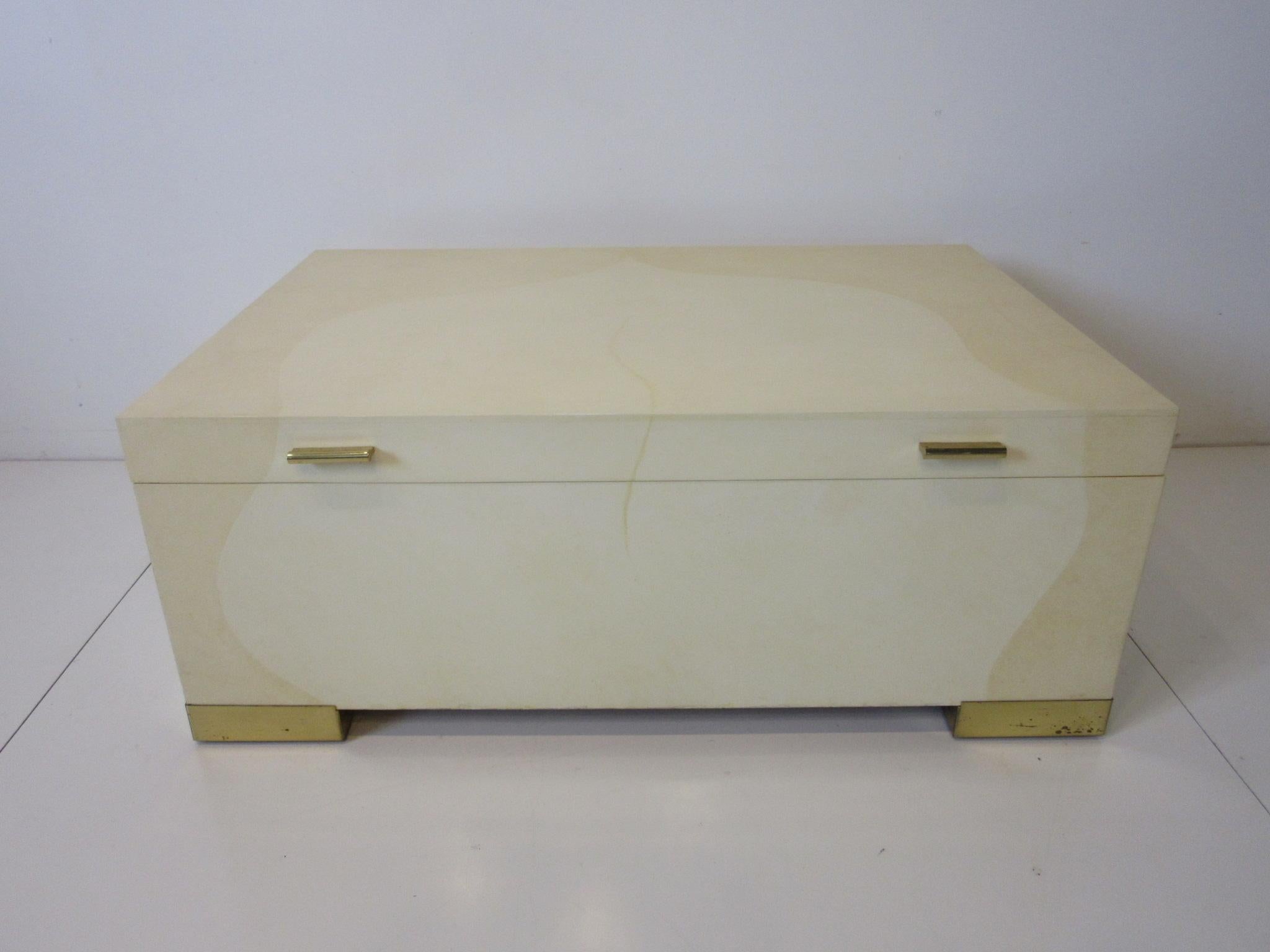 A well crafted coffee table covered in tri colored goatskin / parchment and lacquer having polished brass feet and handles which when opened revels a nice sized storage area. A piece that works as both a coffee table and storage box designed by Karl