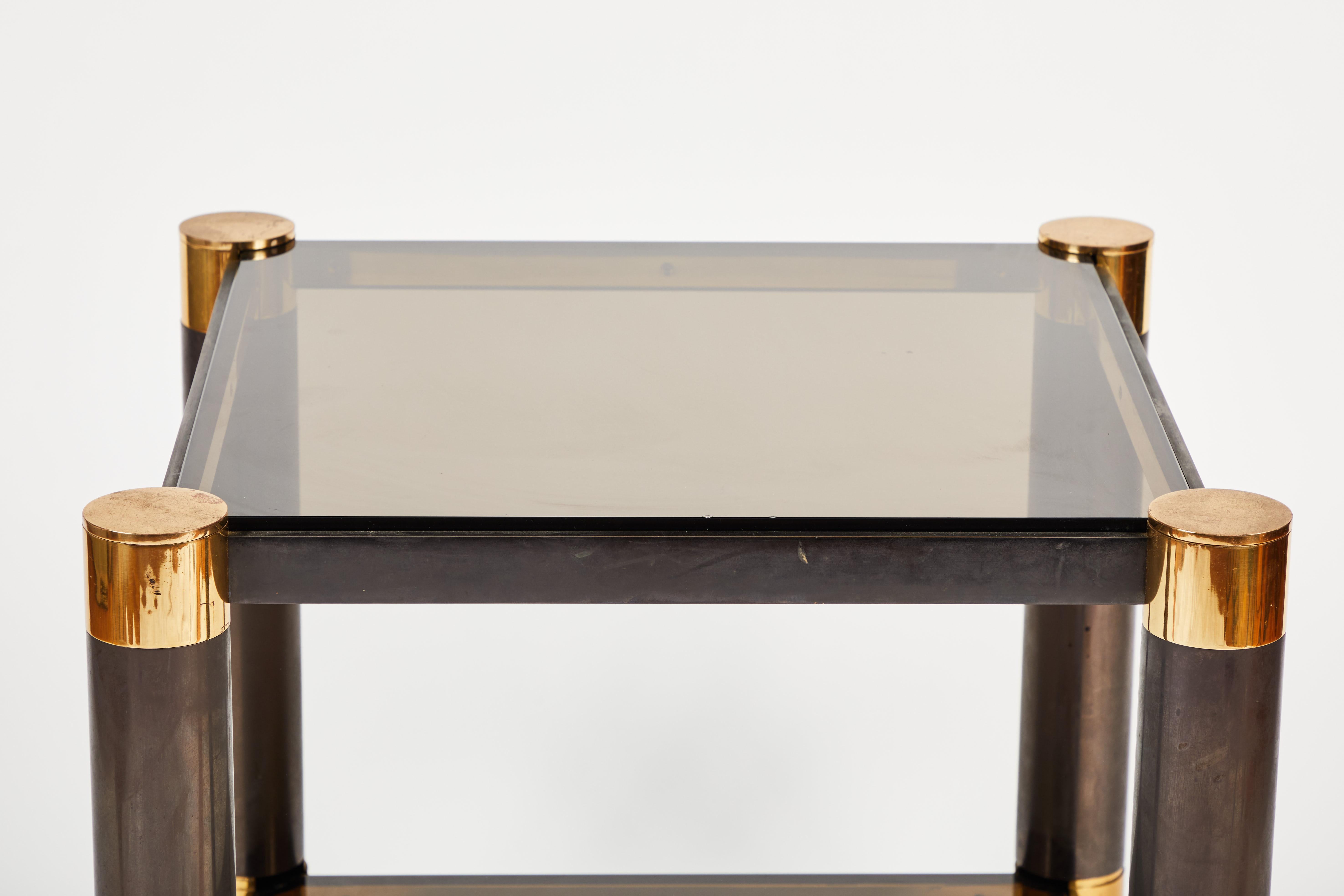 End table by Karl Springer in gunmetal, brass, glass and enameled wood. Crafted in New York circa 1980. This lovely piece has some light oxidation to the gunmetal and brass that is consistent with age. There are some scratches to the glass and light