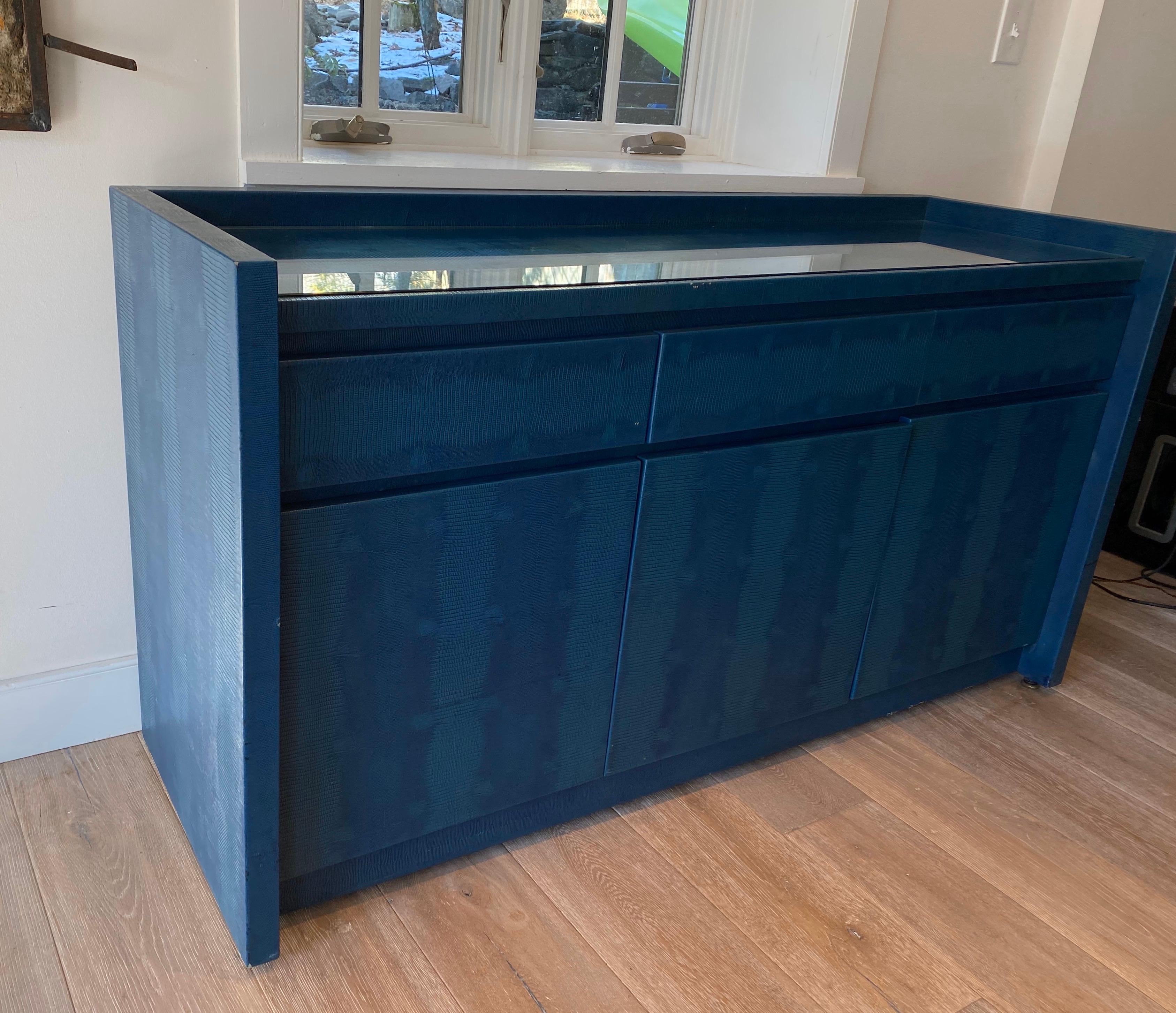 Stunning and rare Karl springer deep blue/ teal lizard skin sideboard. Three lower doors with two shelves and three felt lined drawers above. Complete with inset glass top. The piece is wrapped completely front to back. Signed with leather tab.