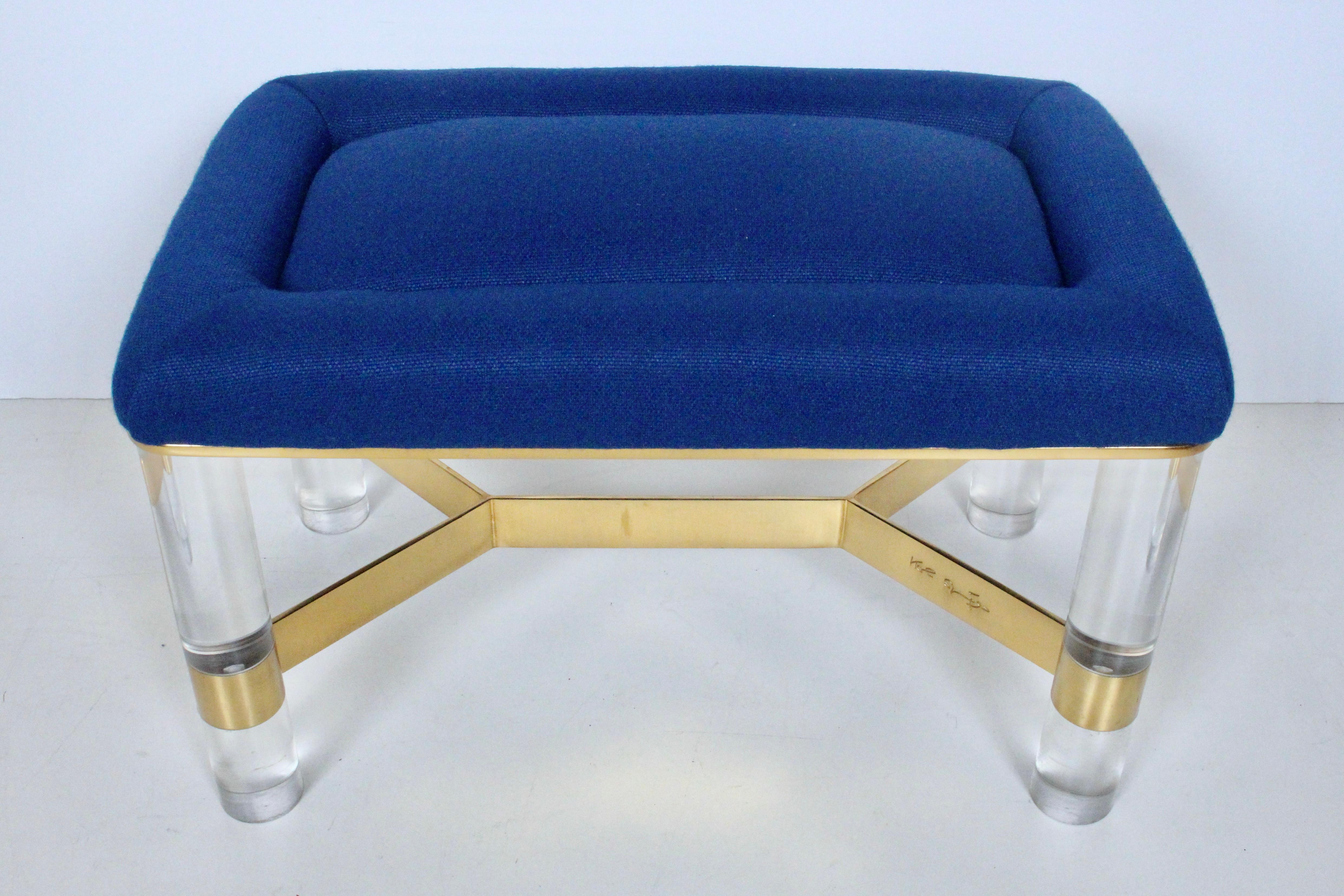 Karl Springer lucite and brass upholstered bench, stool, circa 1980. Featuring a braced rectangular polished brass cross bar frame, four solid cylindrical lucite legs with tufted, luxe woven upholstery. Signed Karl Springer. Kindly note that