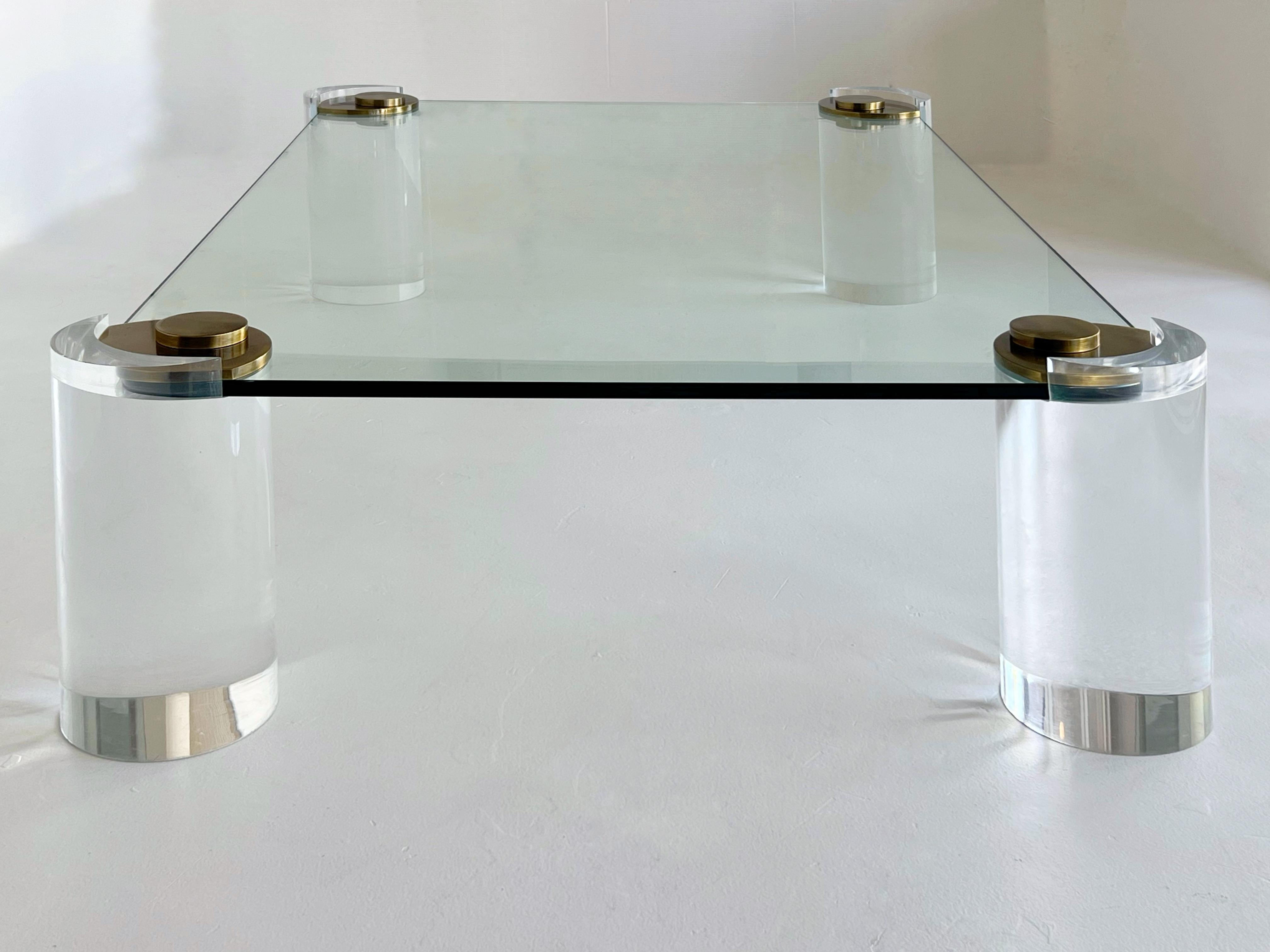 Table basse iconique de Karl Springer, mettant en valeur la maîtrise des matériaux luxueux et des formes sculpturales propres au designer. La table est dotée d'un épais plateau en verre et de pieds architecturaux massifs en Lucite, créant une
