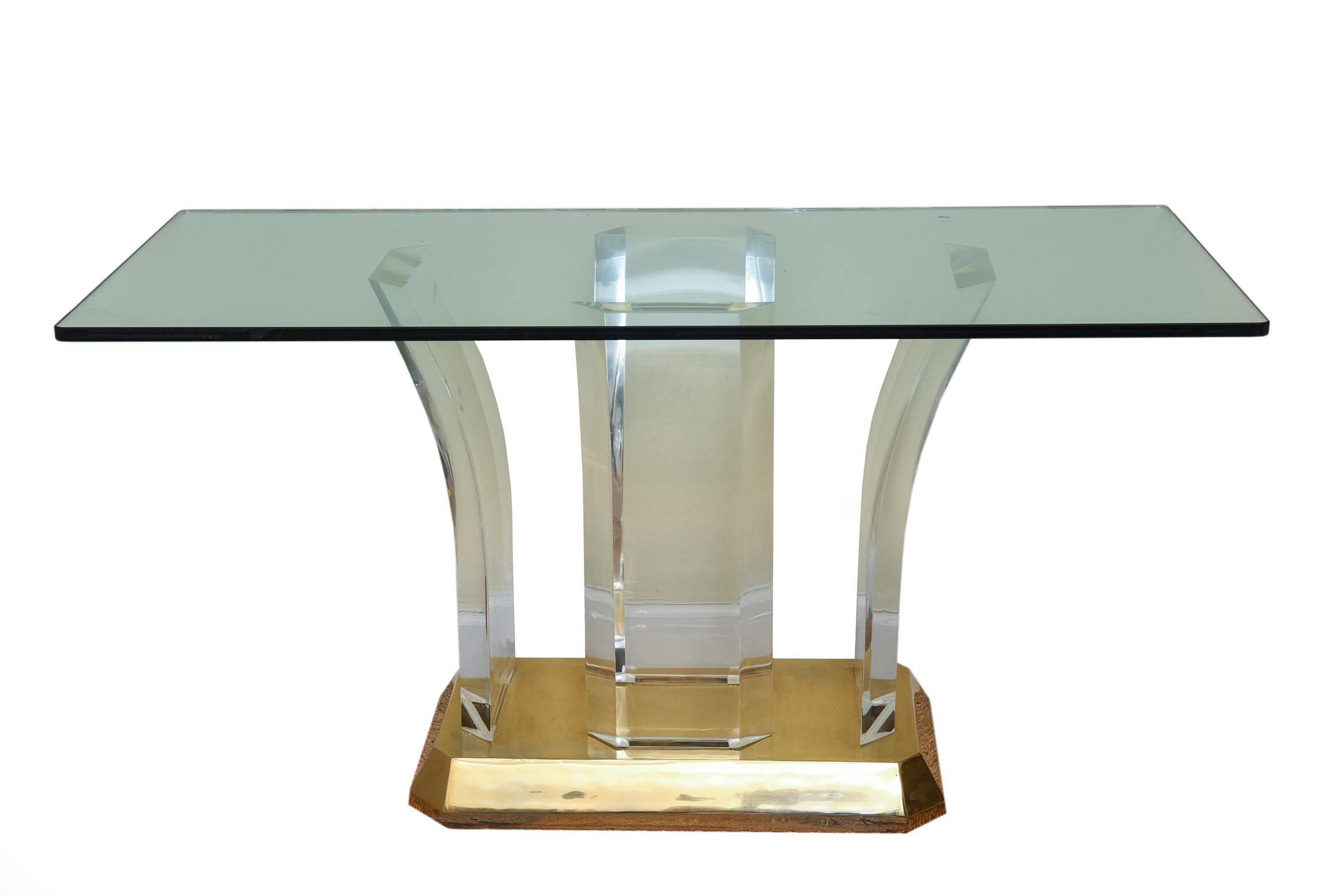 Cette élégante table console vintage Karl Springer, bureau, table d'entrée ou table à manger, est composée de 4 colonnes en lucite arquées qui reposent sur une base en forme de socle angulaire en laiton plaqué or 22 carats. Le dessus est en verre