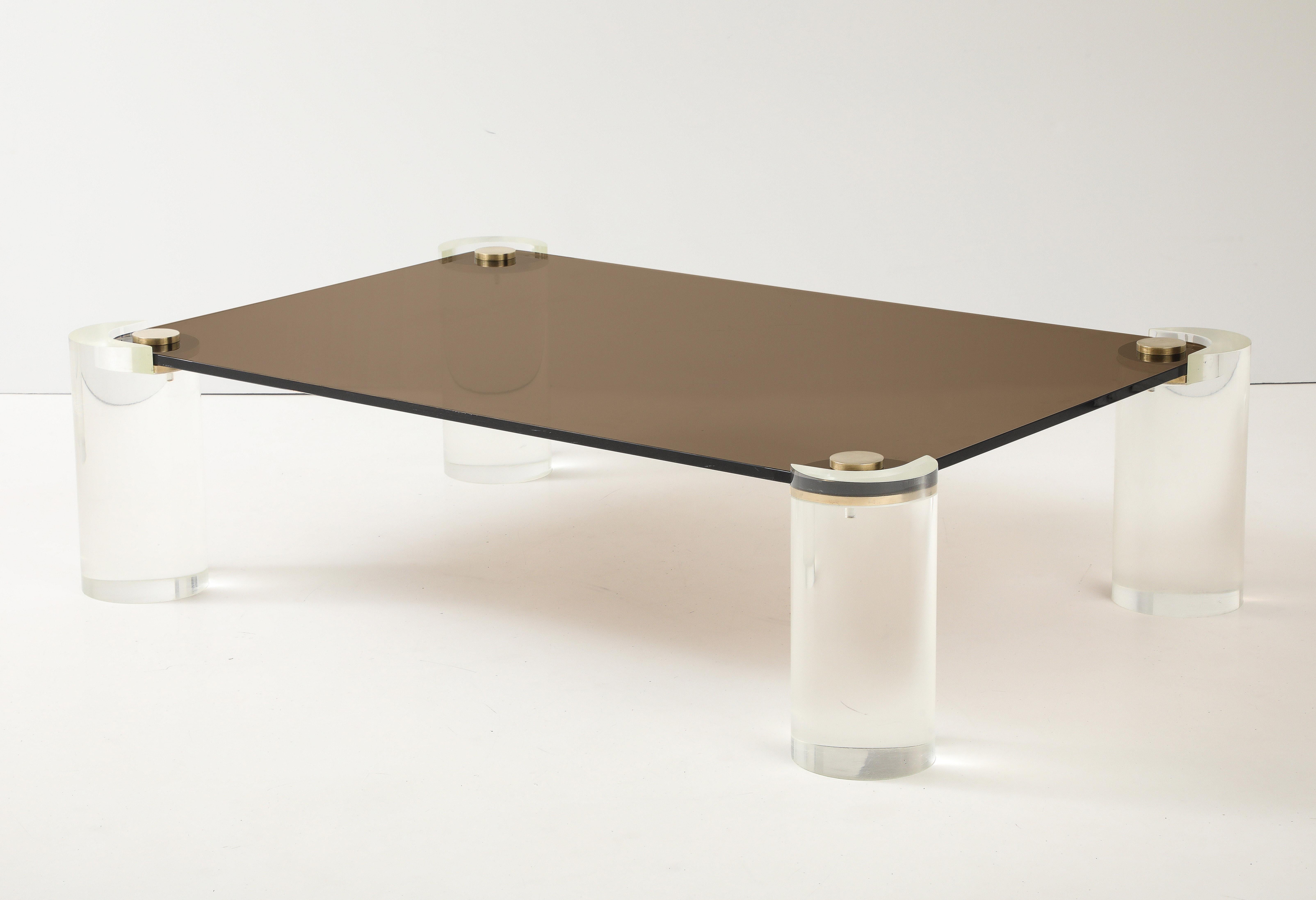 Tavolino rettangolare di grandi dimensioni in lucite e vetro fumé di Karl Springer del 1980.
Quattro colonne in lucite sostengono il vetro affumicato, spesso circa 3,5 cm, che è tenuto in posizione da tappi in ottone lucido.
Il tavolo è in ottime