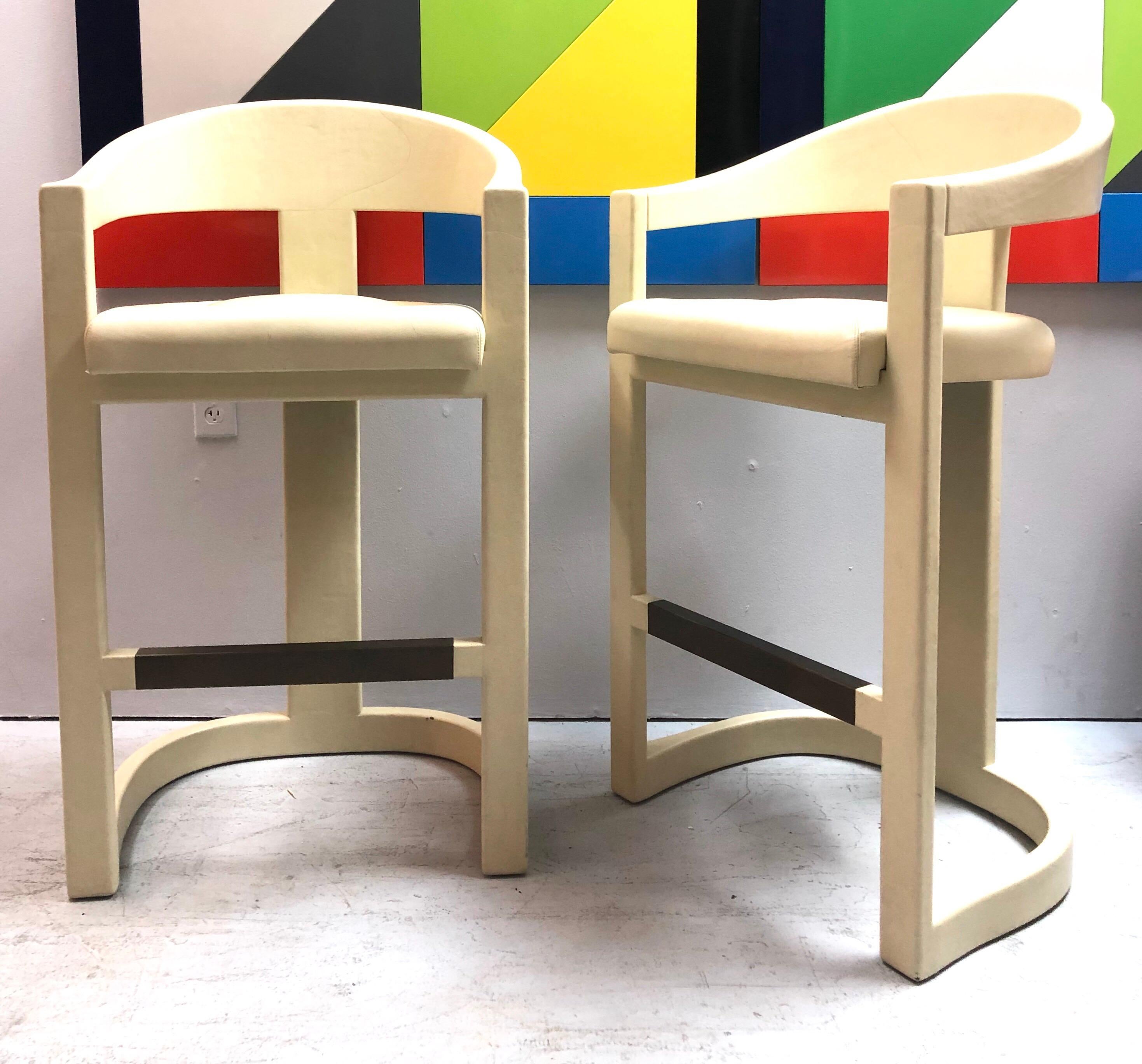 A rare pair of bar stools by Karl Springer. These bar height stools are totally clad in very light neutral bone color leather, same as the seats. The foot rests are brushed antique brass. Very modern-Classic sophisticated look. The leather adds