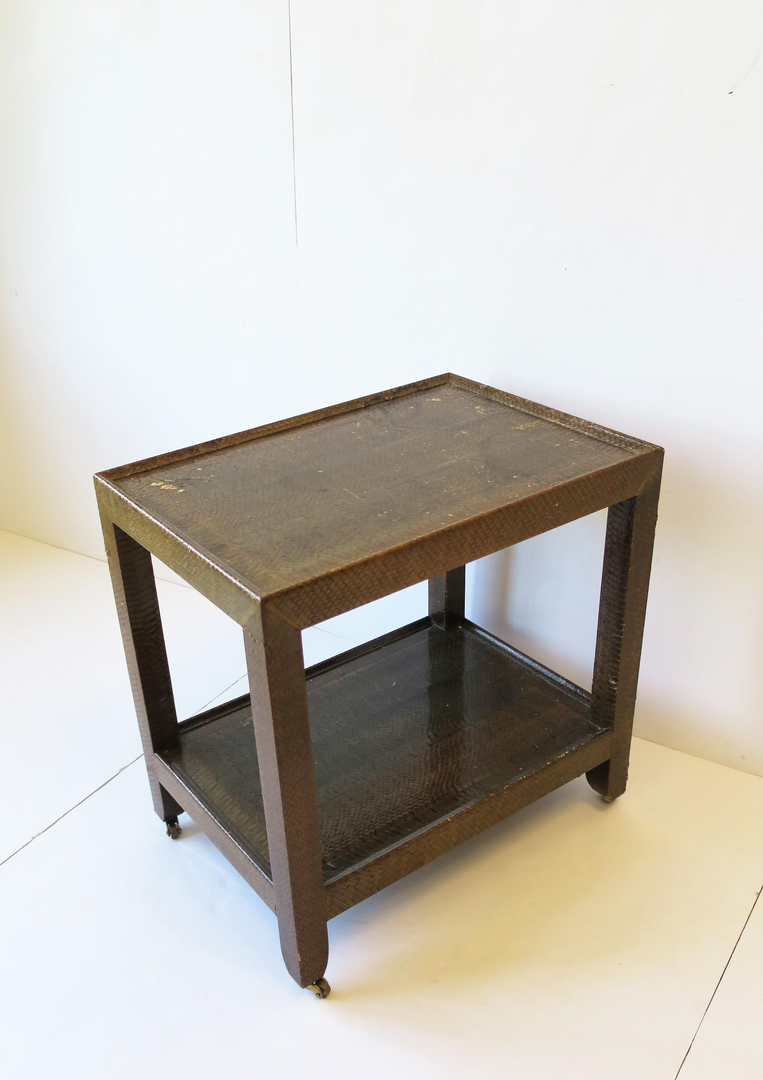A beautiful Postmodern 'telephone' side or end table by designer Karl Springer, 1990. Table is covered in a beautiful authentic snakeskin in a medium brown and supported by small brass caster wheels. Piece is two tiers with lower shelf area for