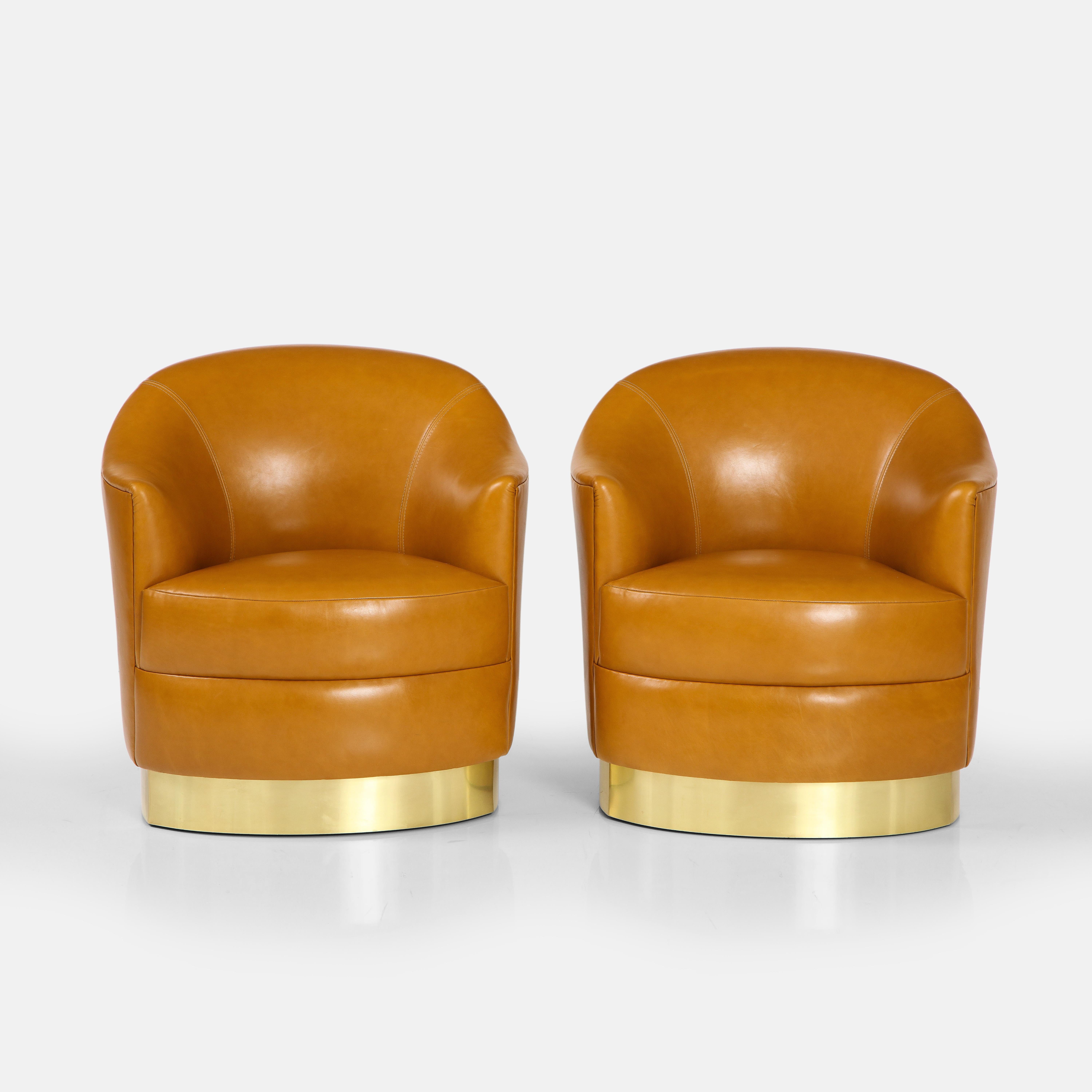 Karl Springer documented rare pair of club chairs in cognac or saddle leather with brass bases, USA, 1980s. This incredibly chic pair of club chairs is more common in the swivel version, but this model is very rare as lounge chairs.  They have