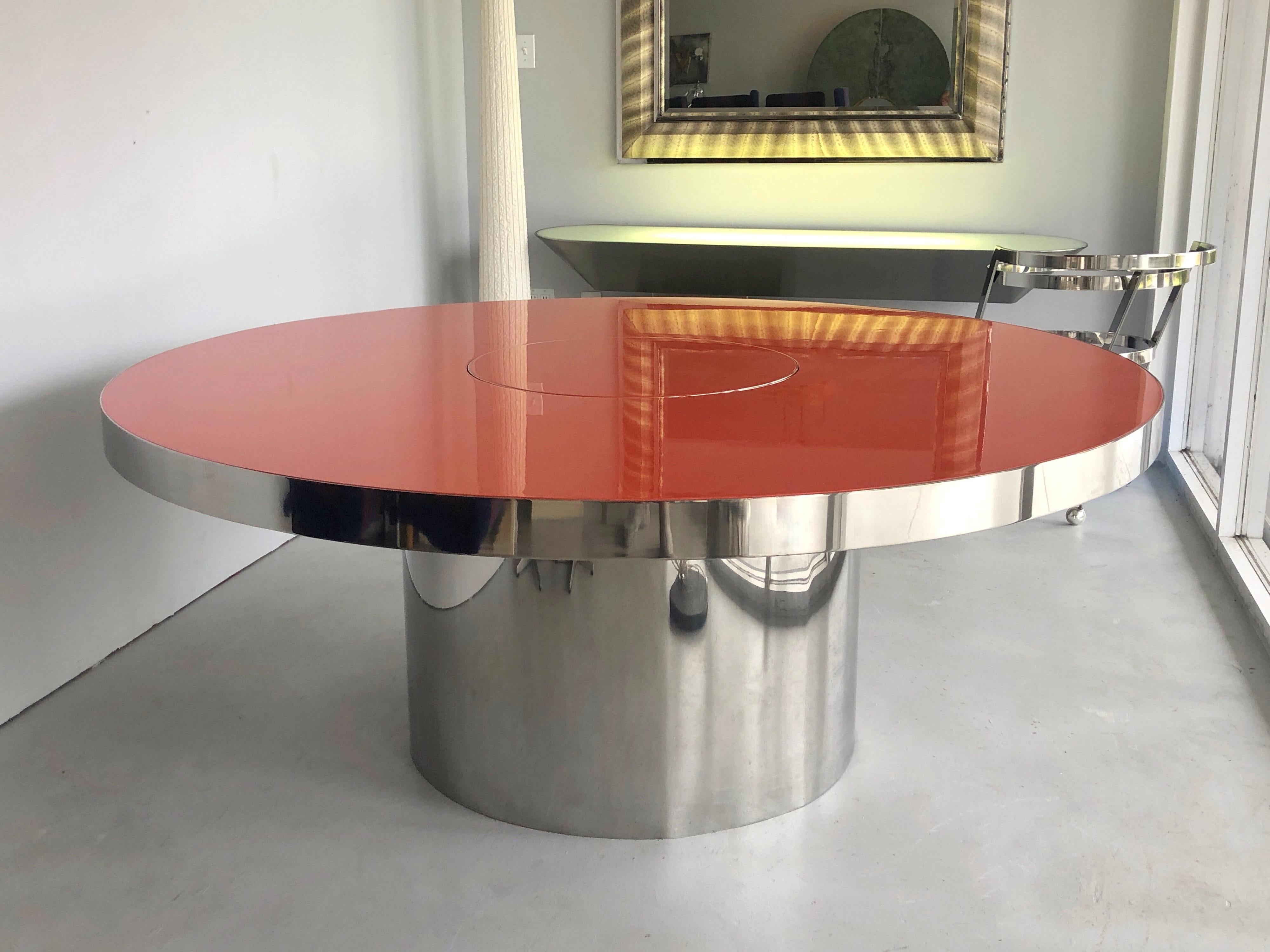 A round dining table. Stainless steel cylindrical base, the top is polished lacquer with a stainless steel border. The small center circle has also a stainless edge and swivels in both directions. Signed with metal tag on verso.