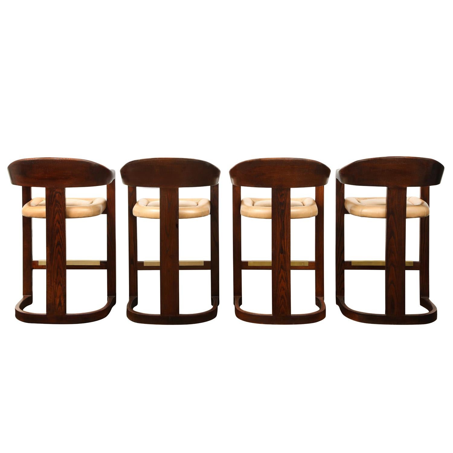 Set of 4 ‘Onassis Bar Stools” in dark oak with upholstered seats and brass foot rests by Karl Springer, American 1980's. Seats are upholstered in leather. The beautiful craftsmanship of these stools makes them very luxurious and