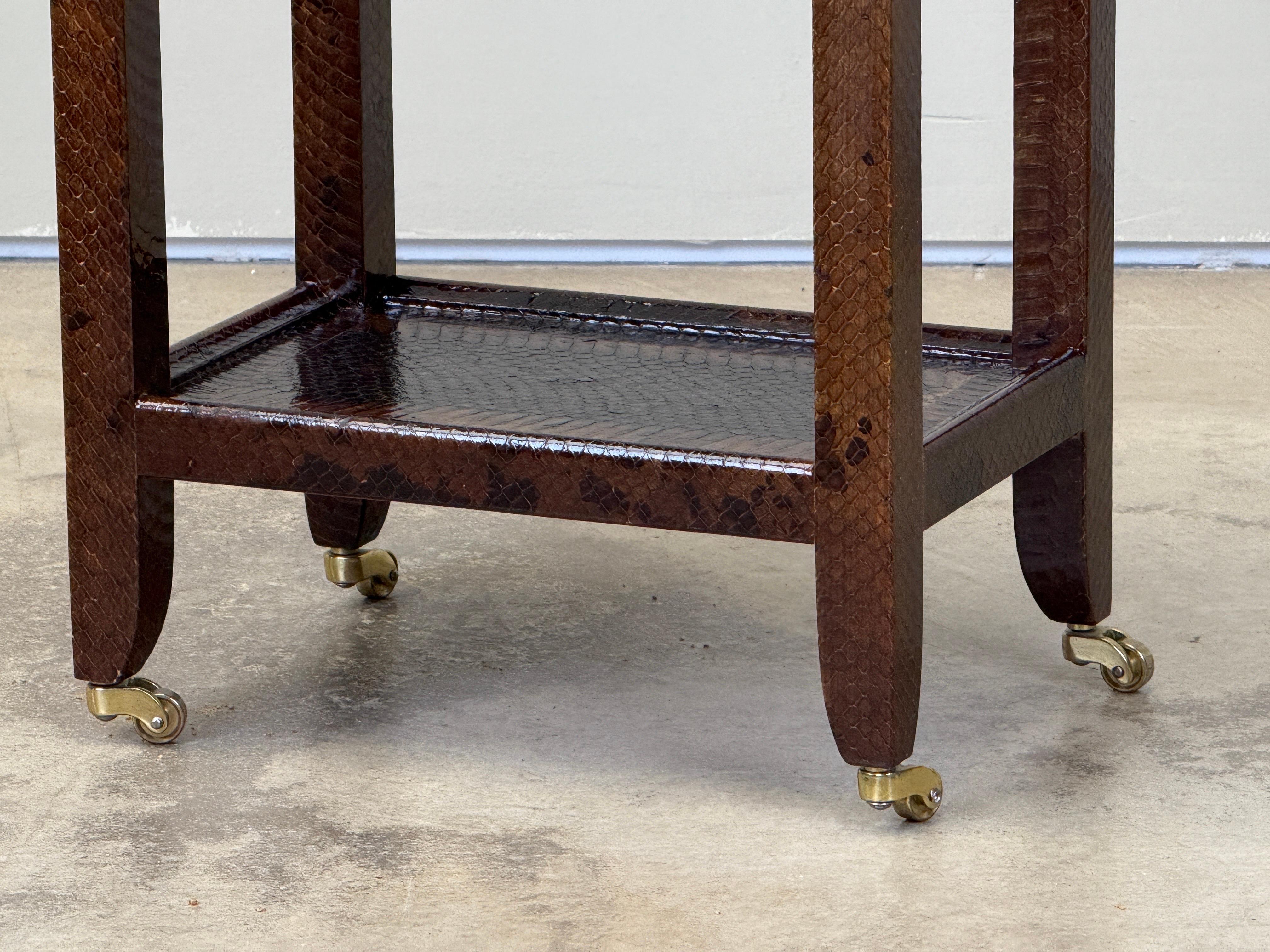 A snake skin covered 'telephone' side table on brass casters by Karl Springer, signed and dated. A second similar table available separately. 