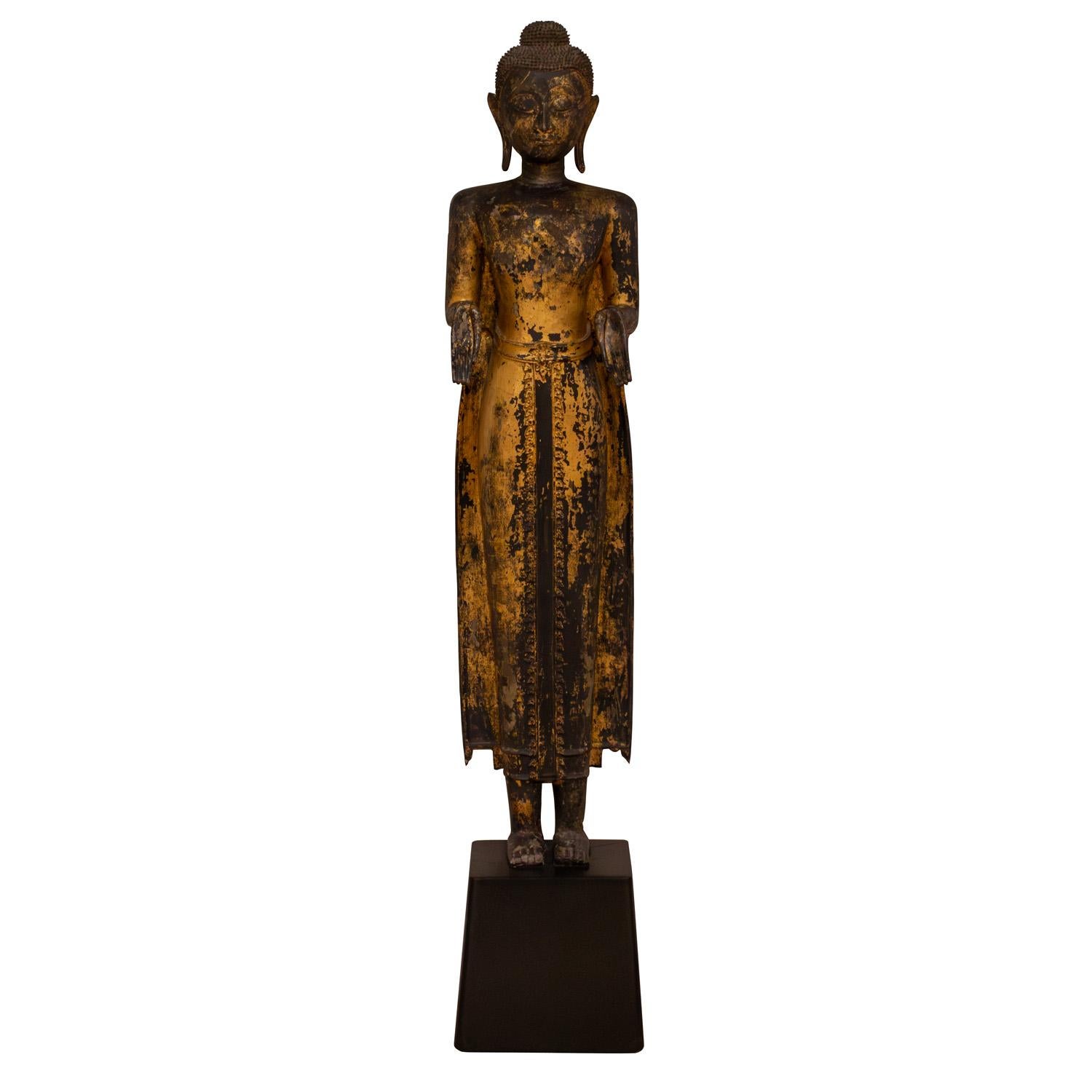 Grande scultura di Buddha in piedi del Siam del XIX secolo, in bronzo dorato, venduta attraverso lo showroom Karl Springer, su una base conica in legno ebanizzato personalizzata da Karl Springer, americano degli anni '80. Le mani della figura sono