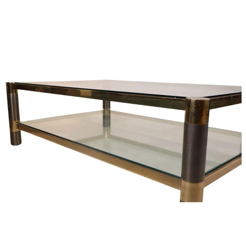 Cette table basse chic à deux niveaux allie harmonieusement la sophistication du milieu du siècle avec une touche du flair distinctif de Karl Springer. Fabriqué avec un cadre en laiton et des pieds circulaires en métal bicolore qui ajoutent de la