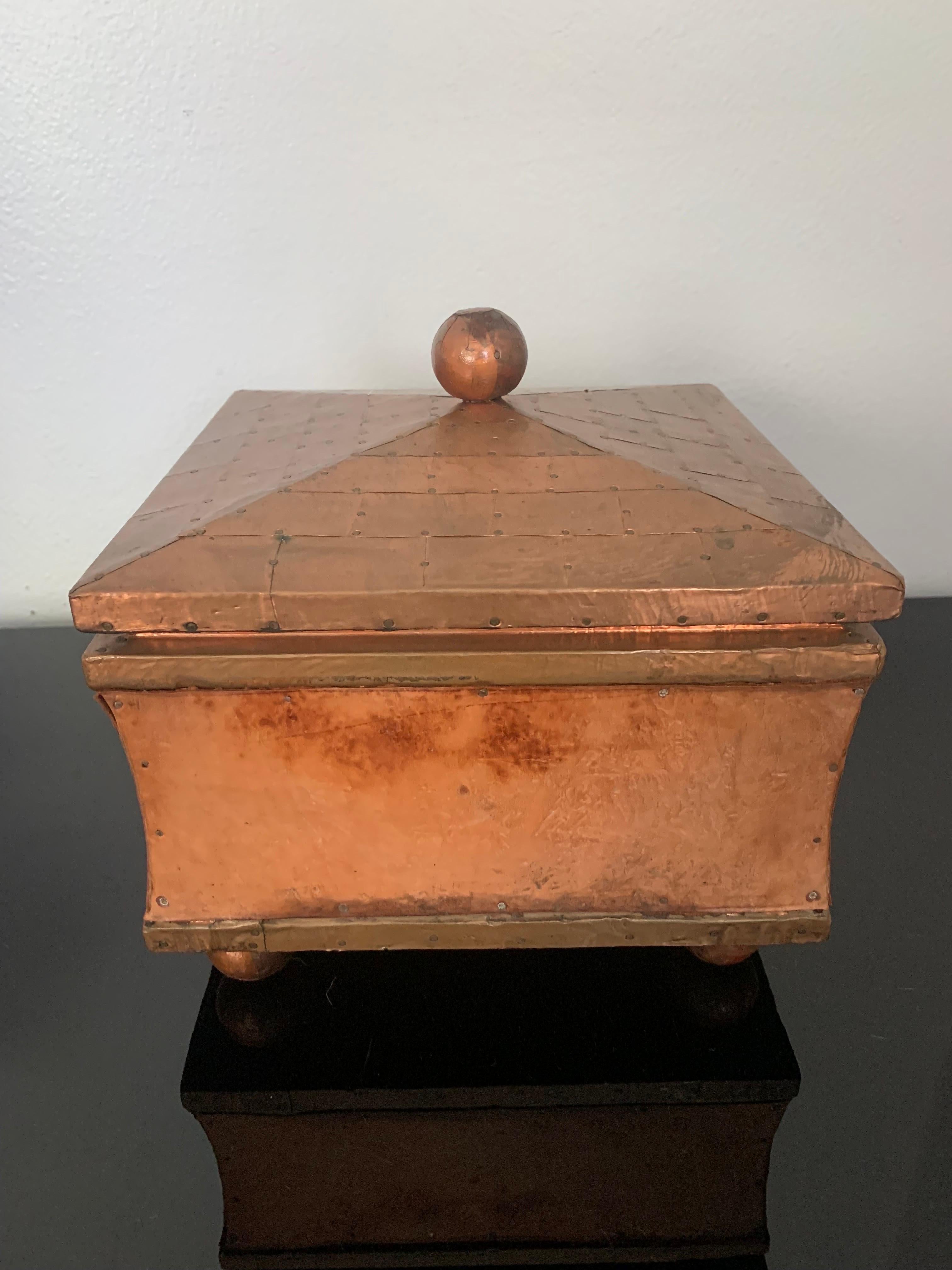 Belle boîte décorative en cuivre et cuir à la manière de Karl Springer. 

Le squelette de la boîte est en bois. Le dessus et les bords sont constitués de carrés de cuivre coupés en bardeaux et fixés par des clous en cuivre. Les côtés de la boîte