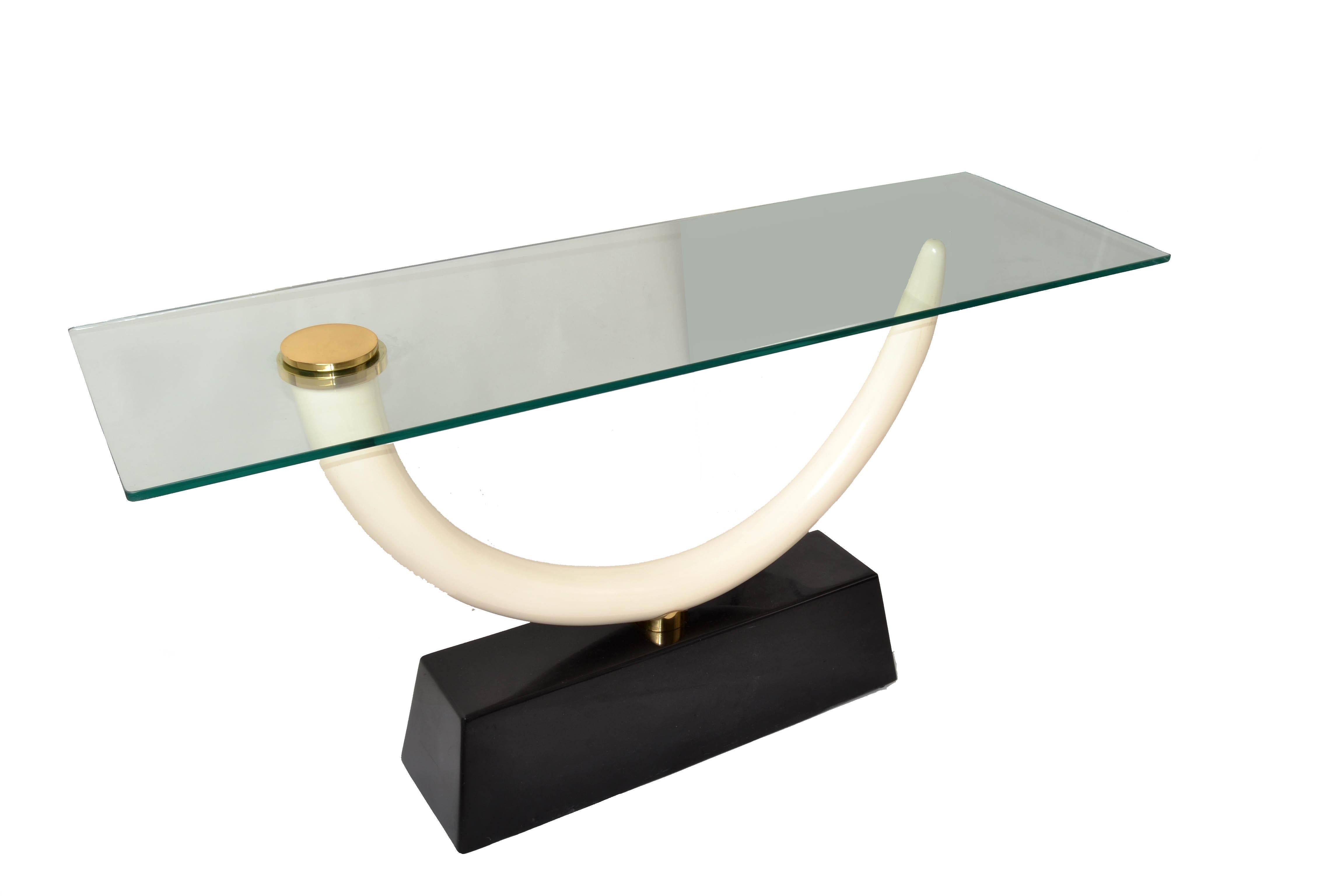 Karl Springer atribuyó a la Mesa Consola un colmillo de imitación marfil que descansa sobre una base de granito lacado en negro. El Colmillo soporta una pesada Tapa de Cristal con bordes redondeados y se monta mediante un Disco de Bronce que hace