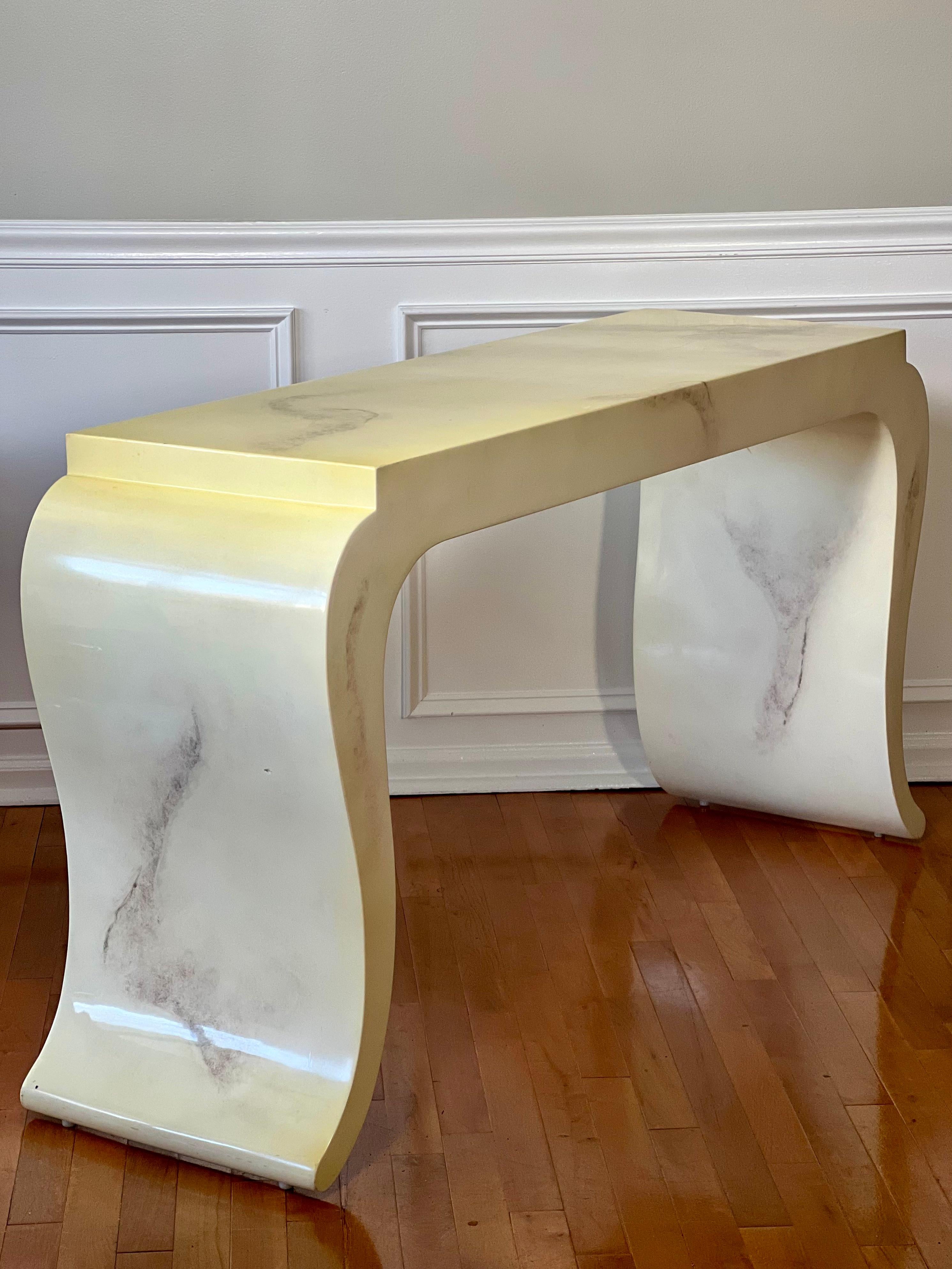Elegant and curvaceous vintage console table in the manner of Karl Springer.

The table features a faux marble lacquer finish throughout in creamy white, gray and light brown depicting natural color variations found in real stone. A gorgeous table