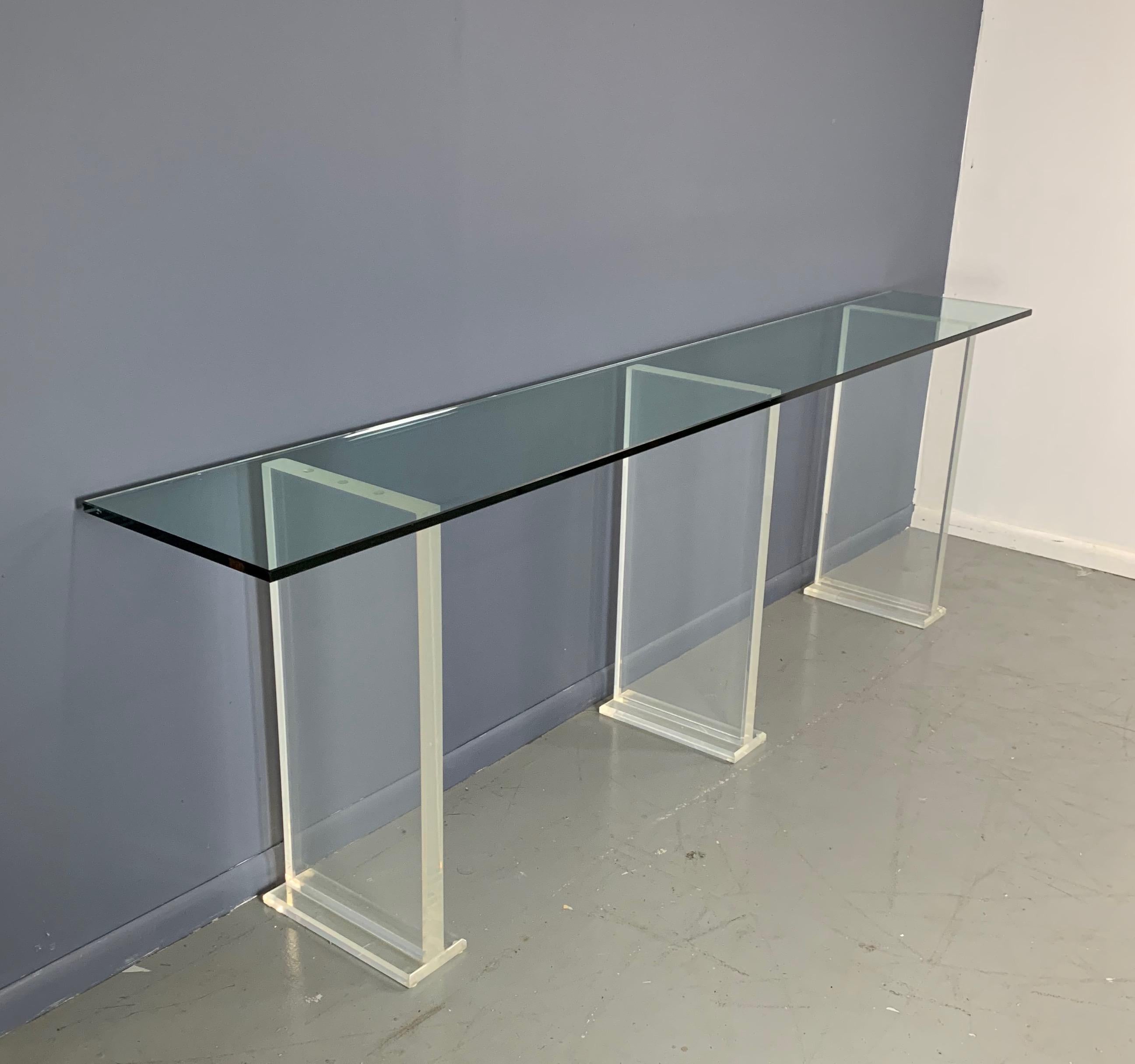 Even though this massive glass and Lucite console is prodigious in size, the Lucite legs lend the piece a lightness that makes it seem like the glass is floating in air. These Lucite legs are very substantial and give this very long table stability.