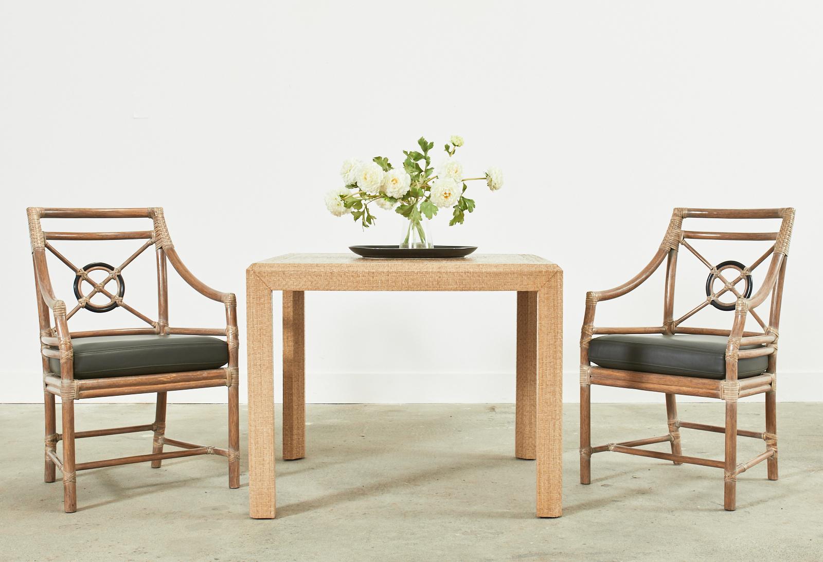 Stylish square dining table or breakfast table featuring a lacquered raffia grasscloth clad frame. Made in the style and manner of Karl Springer and Harrison Van-Horn. The parsons style table has a decorative brass inlay square on the top and a