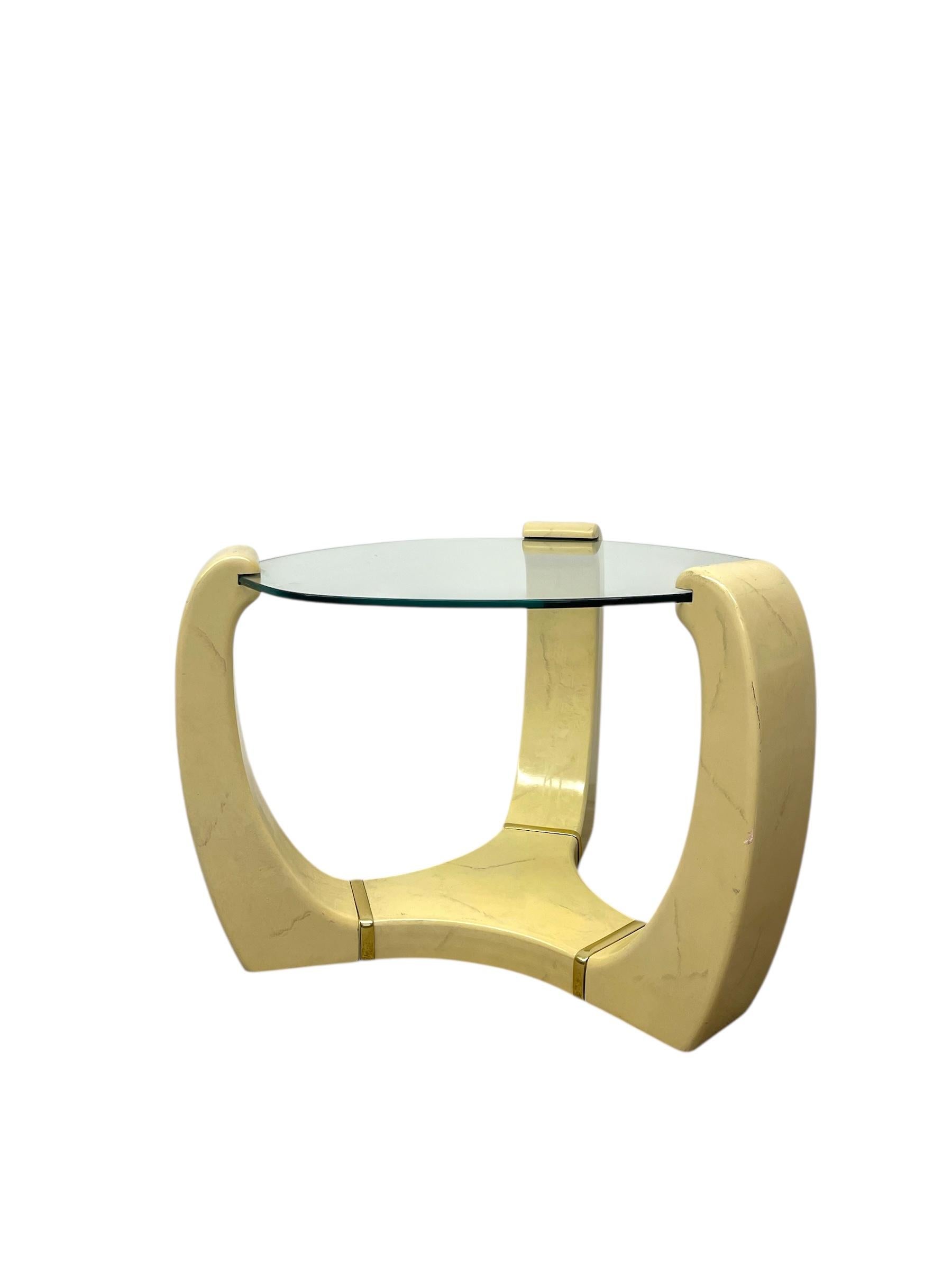 Escultural mesa auxiliar de estilo Karl Springer con base trípode y detalles incrustados en latón. La base está acabada en un tono crema claro con un sutil veteado, que le da la apariencia del mármol al tiempo que mantiene un elegante perfil